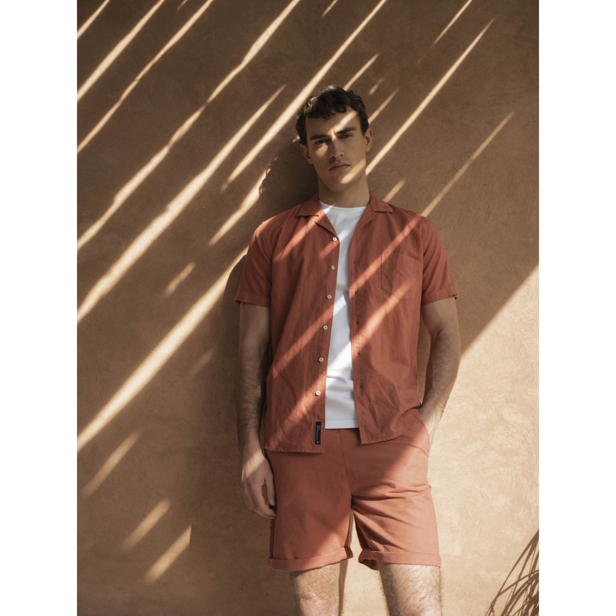 Man wearing a matching outfit of a shirt and shorts against a textured wall.