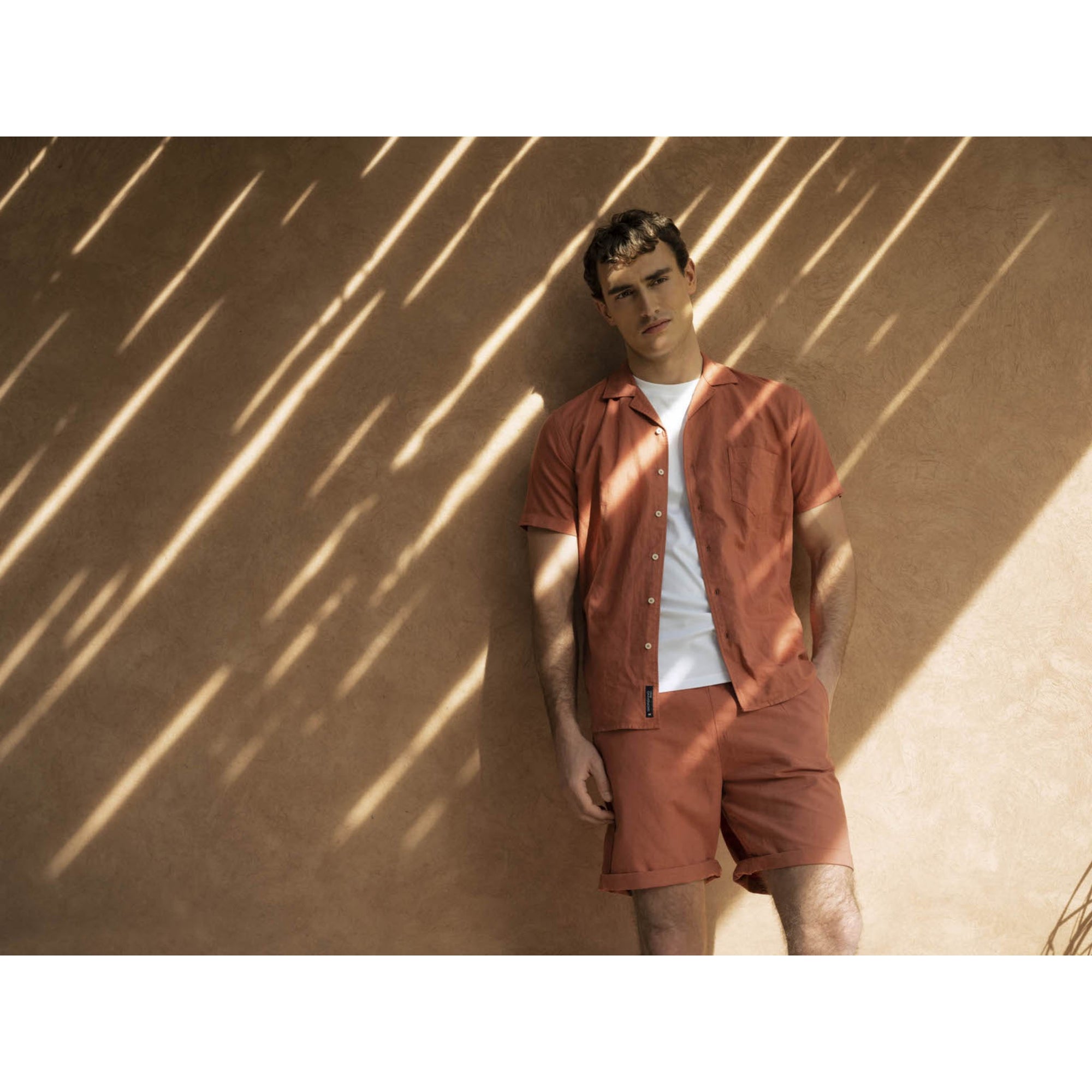 Man wearing a matching outfit of a shirt and shorts against a textured wall.