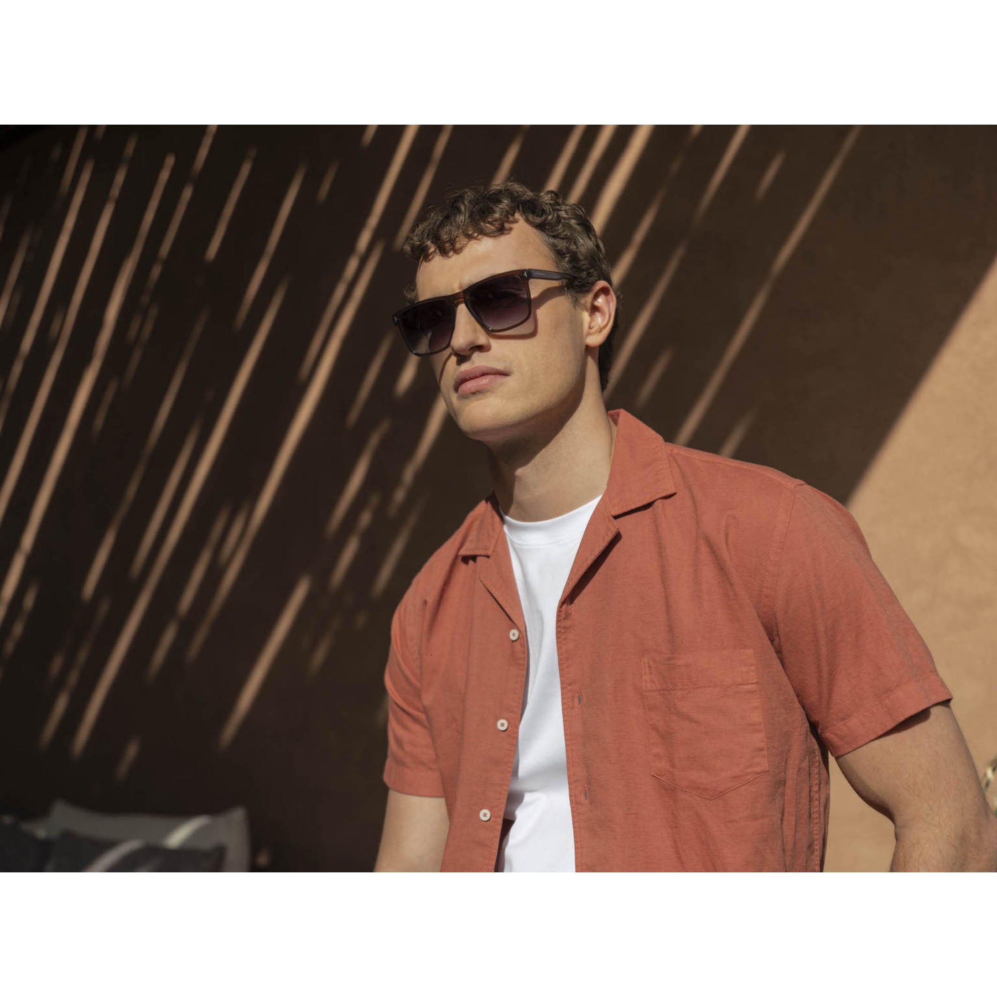 Man wearing sunglasses and a red shirt against a textured wall