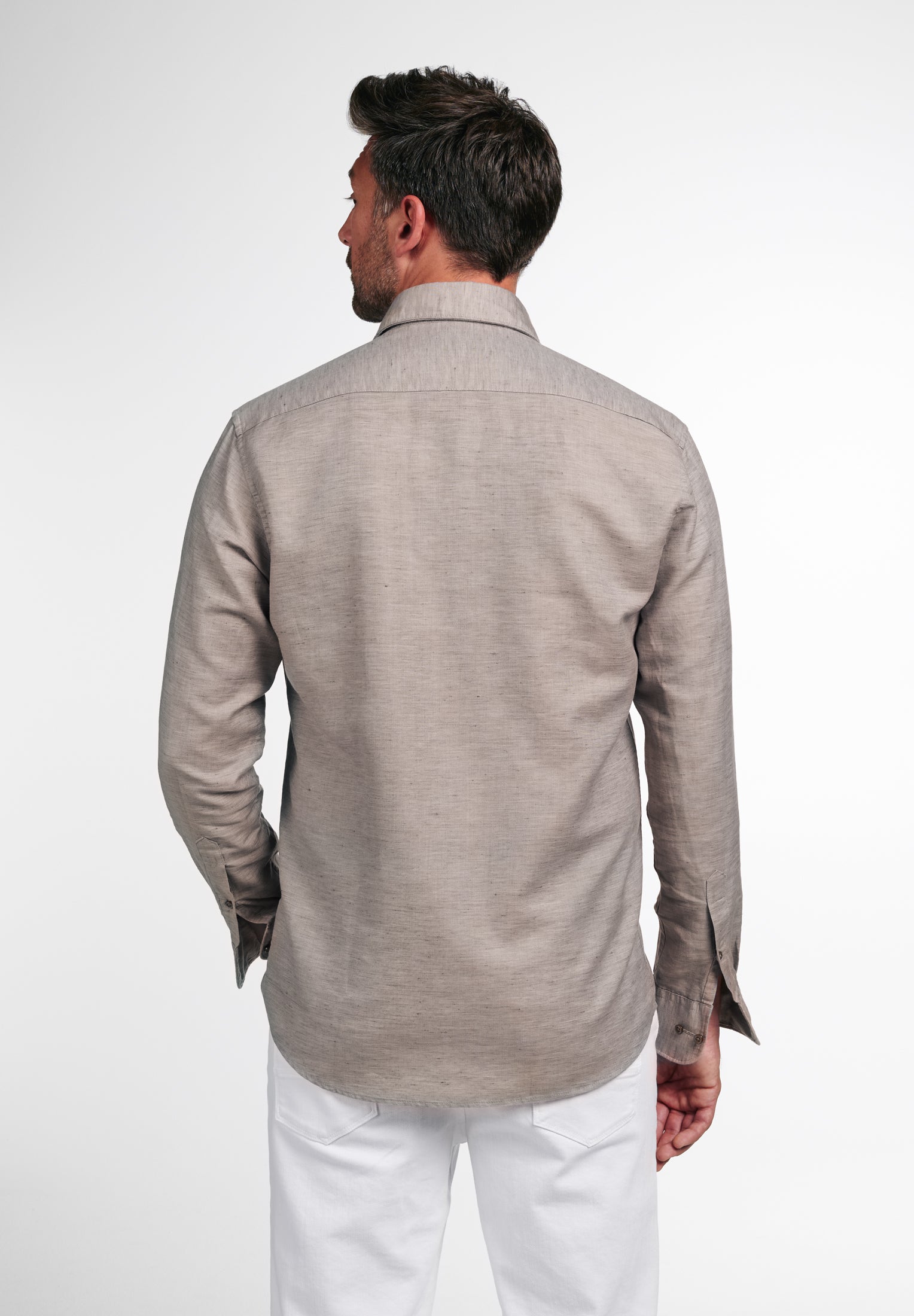 Man wearing a beige jacket and white pants on a white background