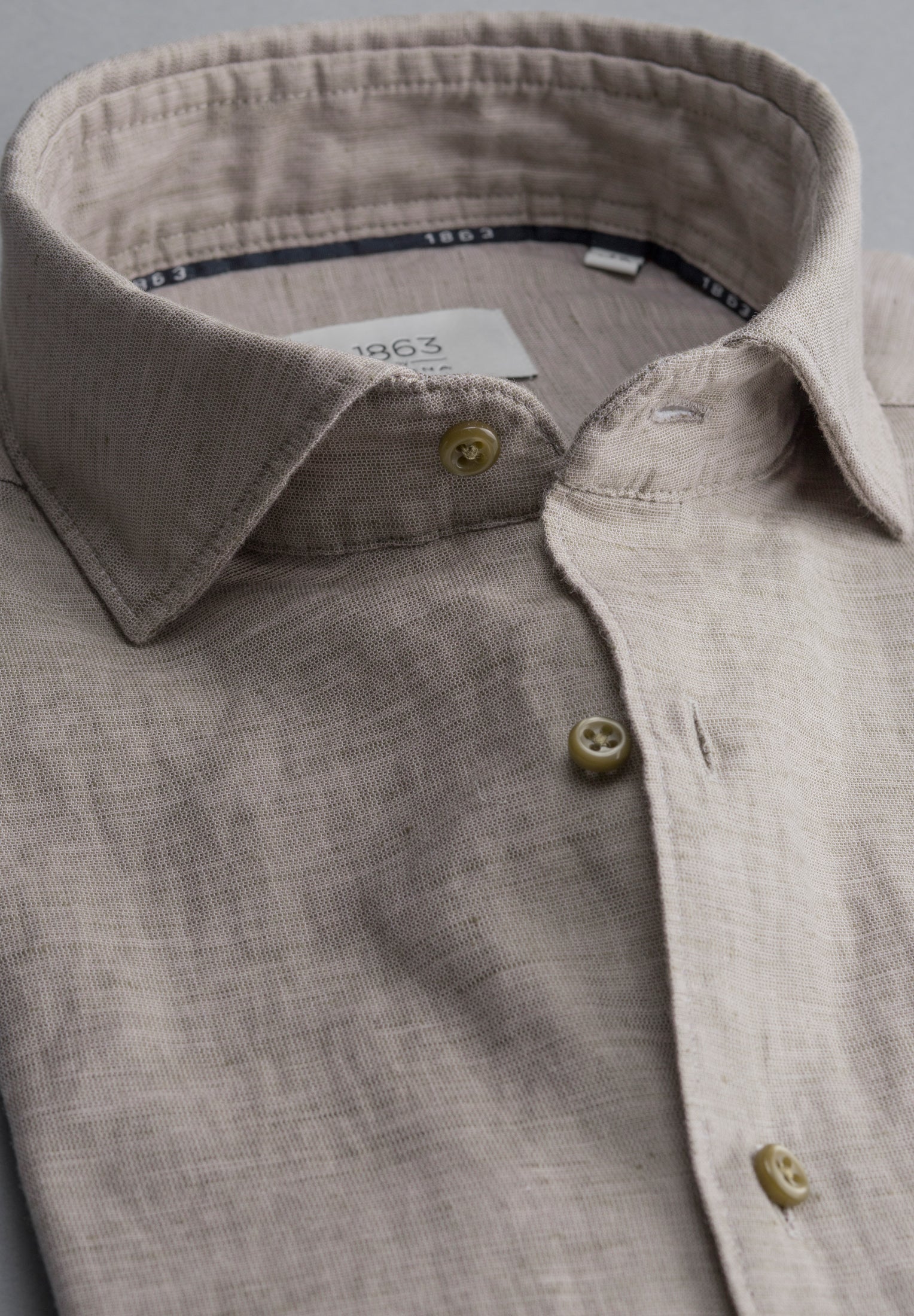 Close-up of a light gray shirt with collar and buttons, brand label visible.