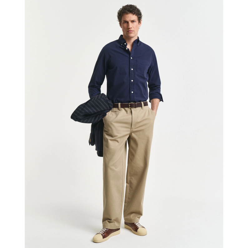 Man wearing a navy GANT shirt and beige pants holding a dark jacket on a white background