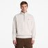 A man wearing a cream-colored Timberland quarter-zip pullover sweater with a small embroidered logo on the left chest, paired with brown pants, against a plain white background.