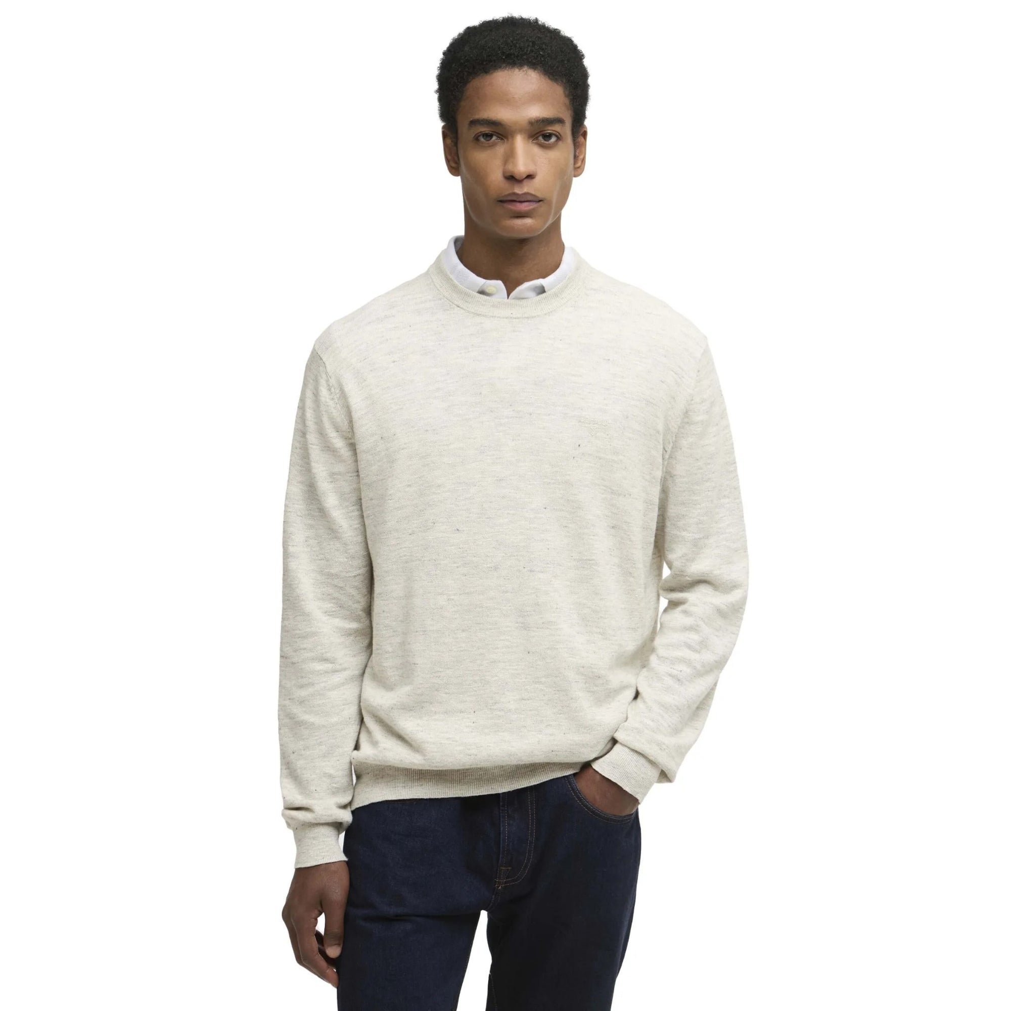 Man wearing a light gray sweater over a white shirt with dark pants on a white background