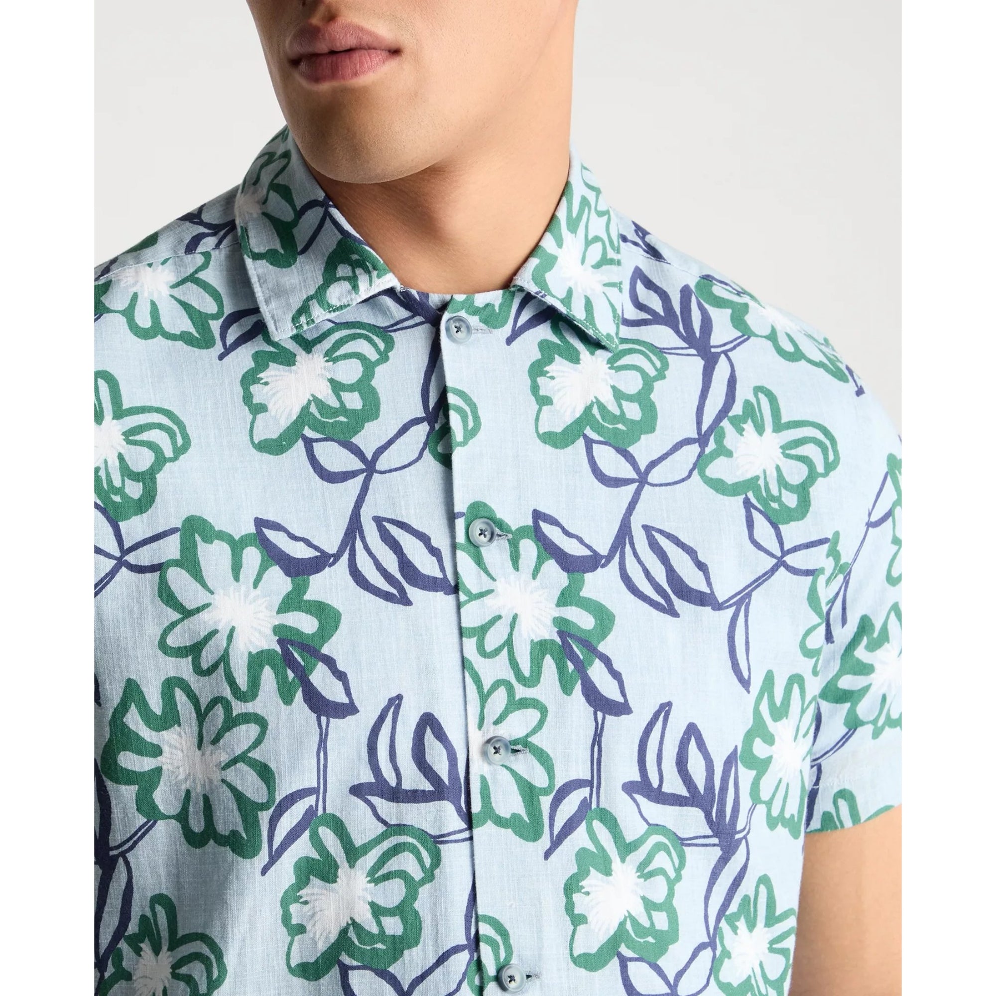 Close-up of a person wearing a floral patterned shirt with green and purple leaves on a light blue background.
