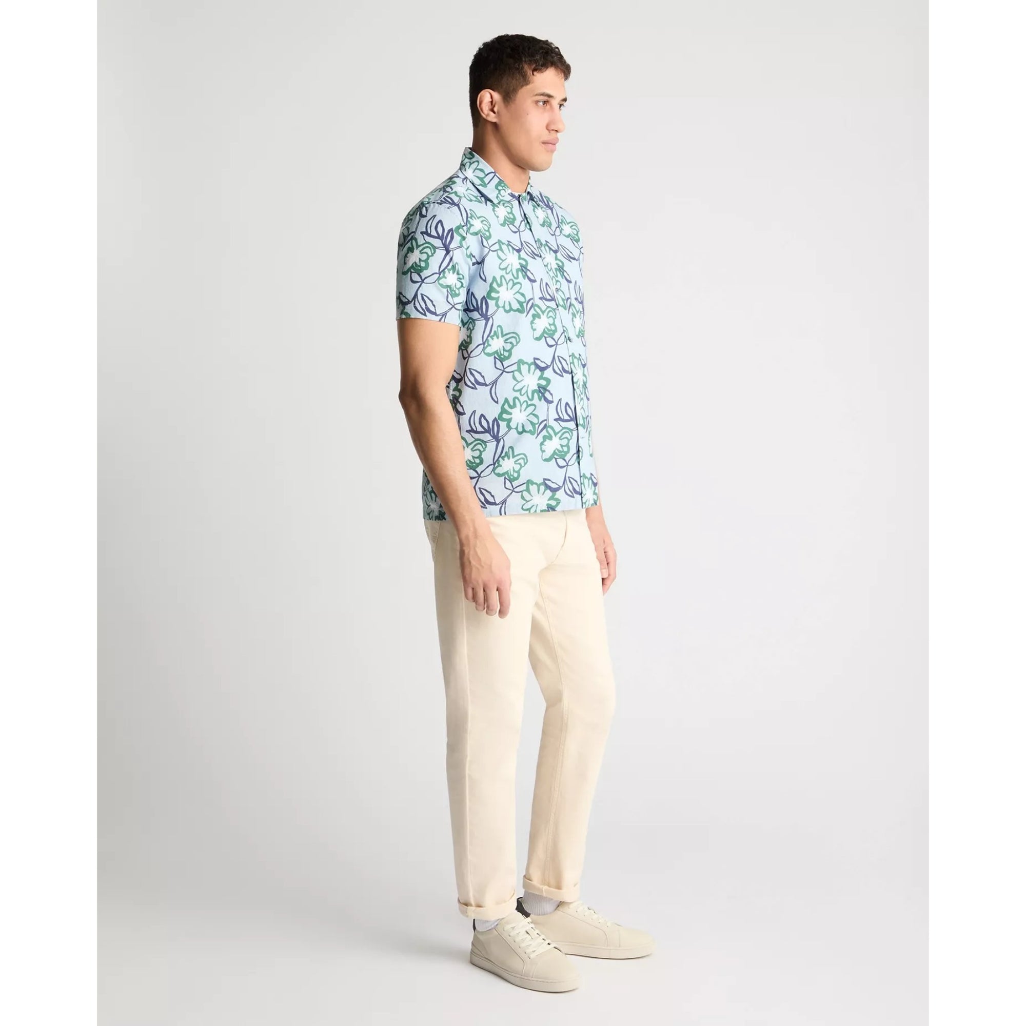 Man wearing a patterned shirt and beige pants on a white background
