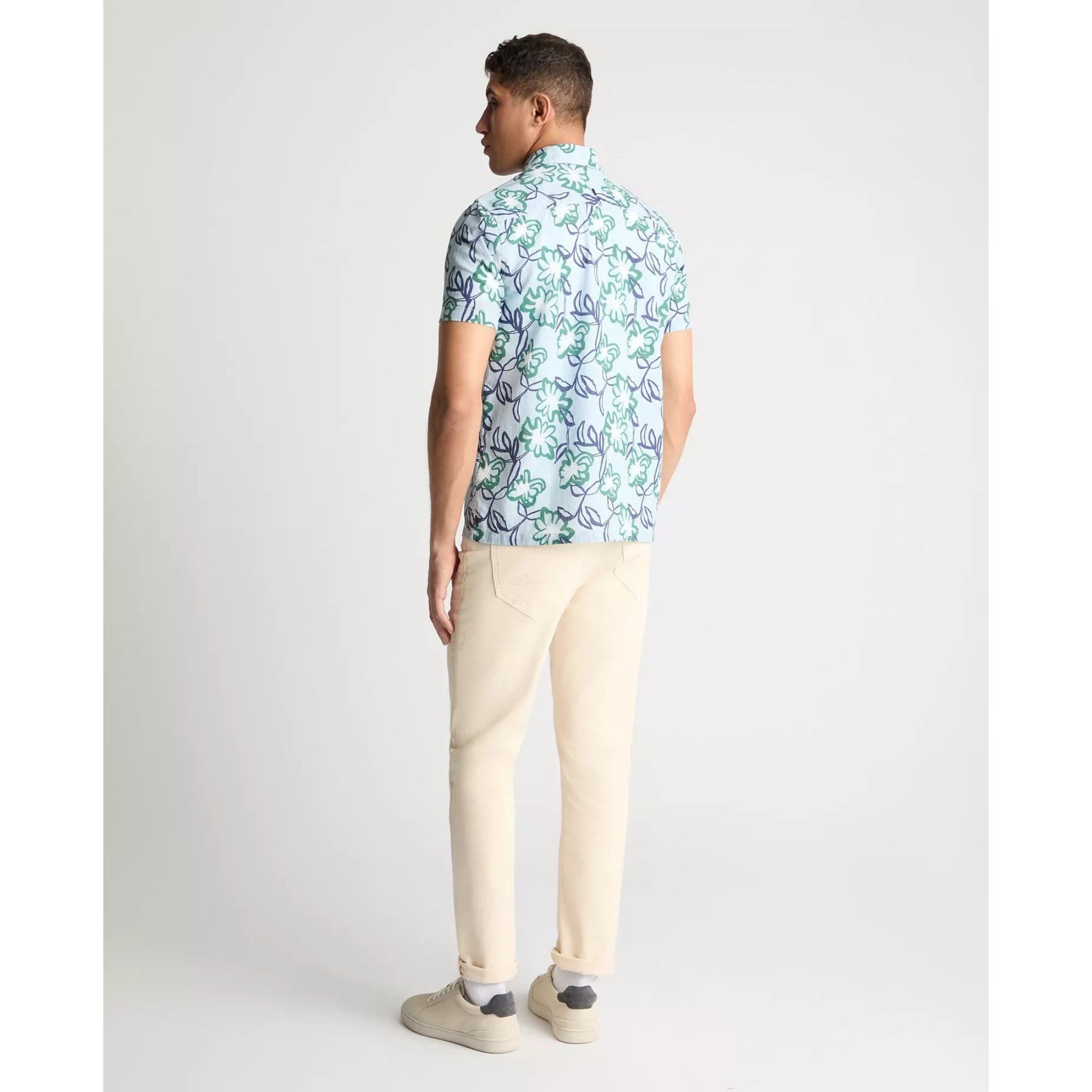 Man wearing a patterned shirt and beige pants on a white background