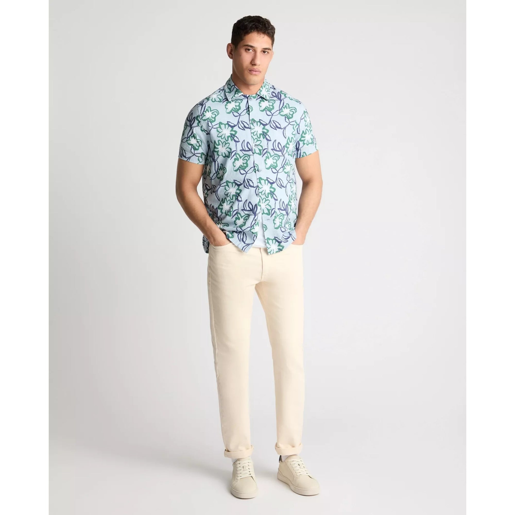 Man wearing a patterned shirt and beige pants on a white background