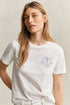 Woman wearing a white t-shirt with a small logo on a beige background