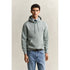 Man wearing a light gray hoodie and blue jeans against a beige background
