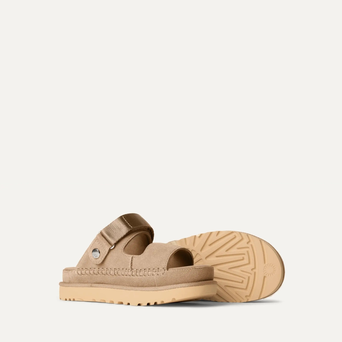 A pair of UGG Goldenstar Glide sandals in sand color with an adjustable heel strap and a low heel.