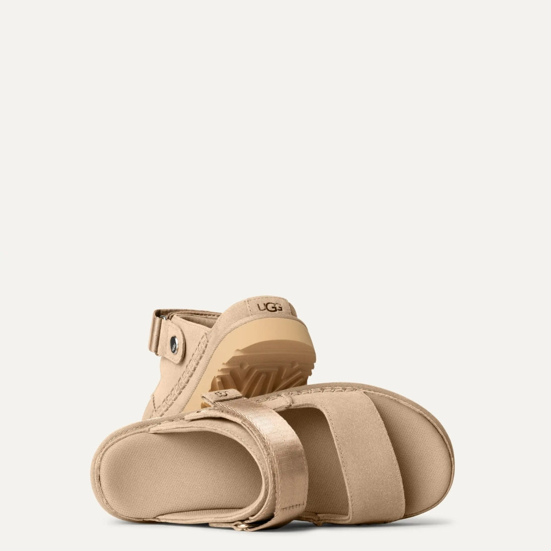 A pair of UGG Goldenstar Glide sandals in sand color with an adjustable heel strap and a low heel.