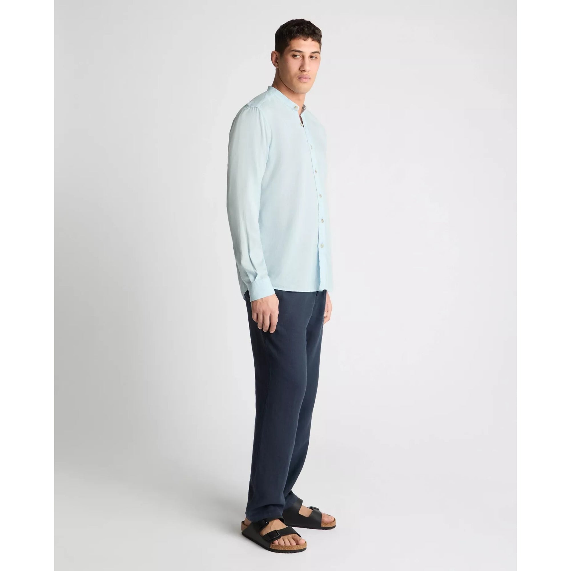 Man wearing a light blue shirt and dark pants on a white background