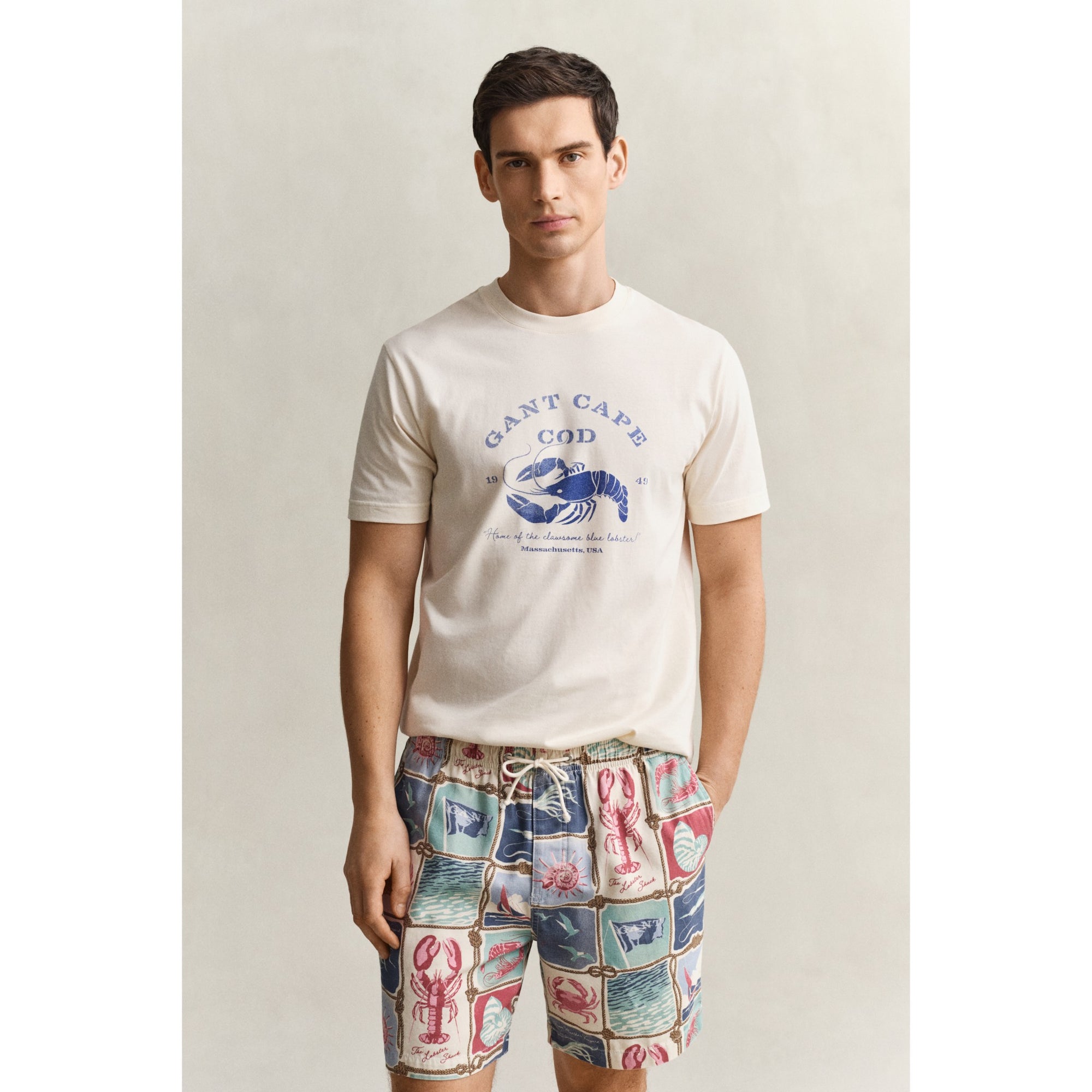 Man wearing a graphic t-shirt and patterned shorts on a plain background