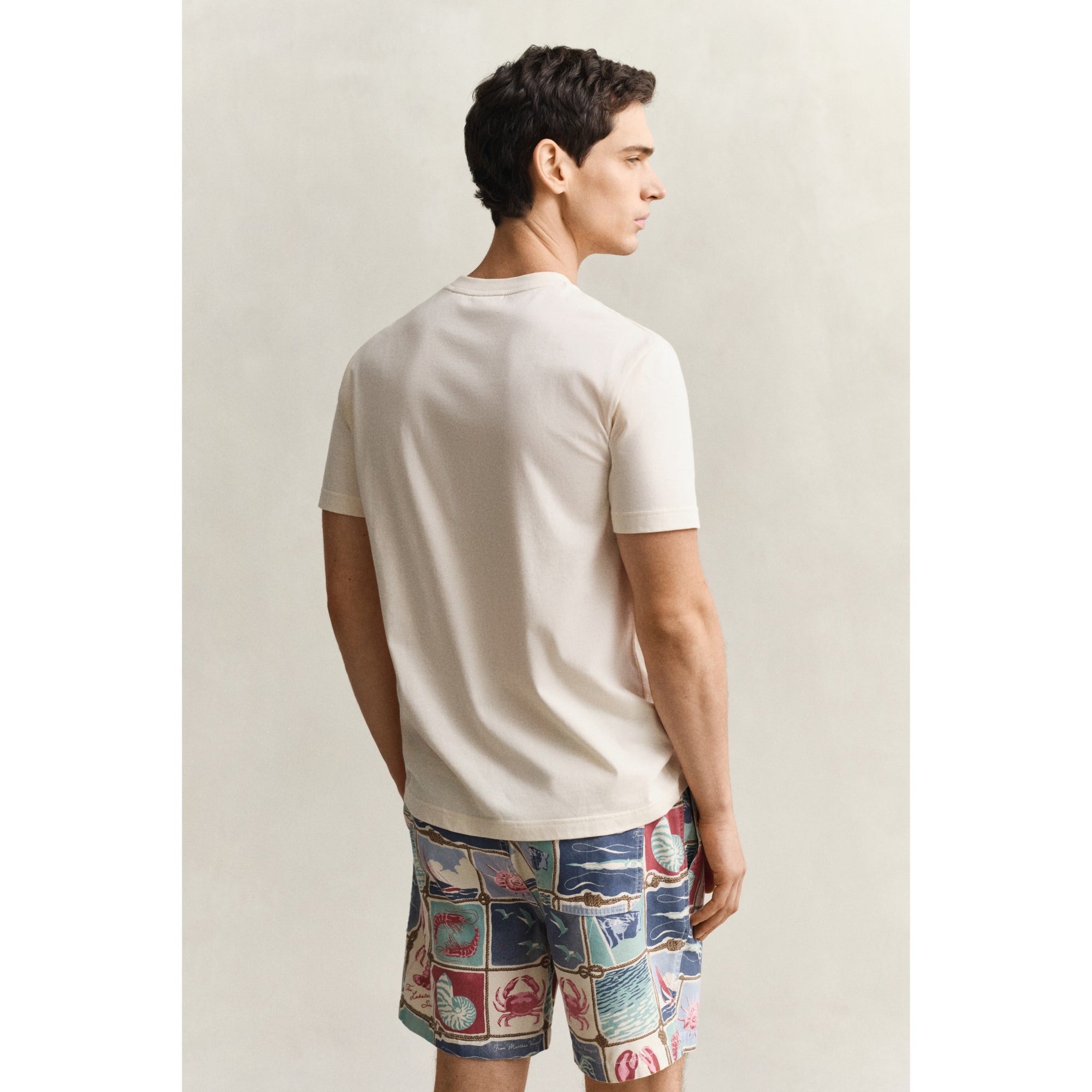 Man wearing a white t-shirt and colorful patterned shorts on a plain background