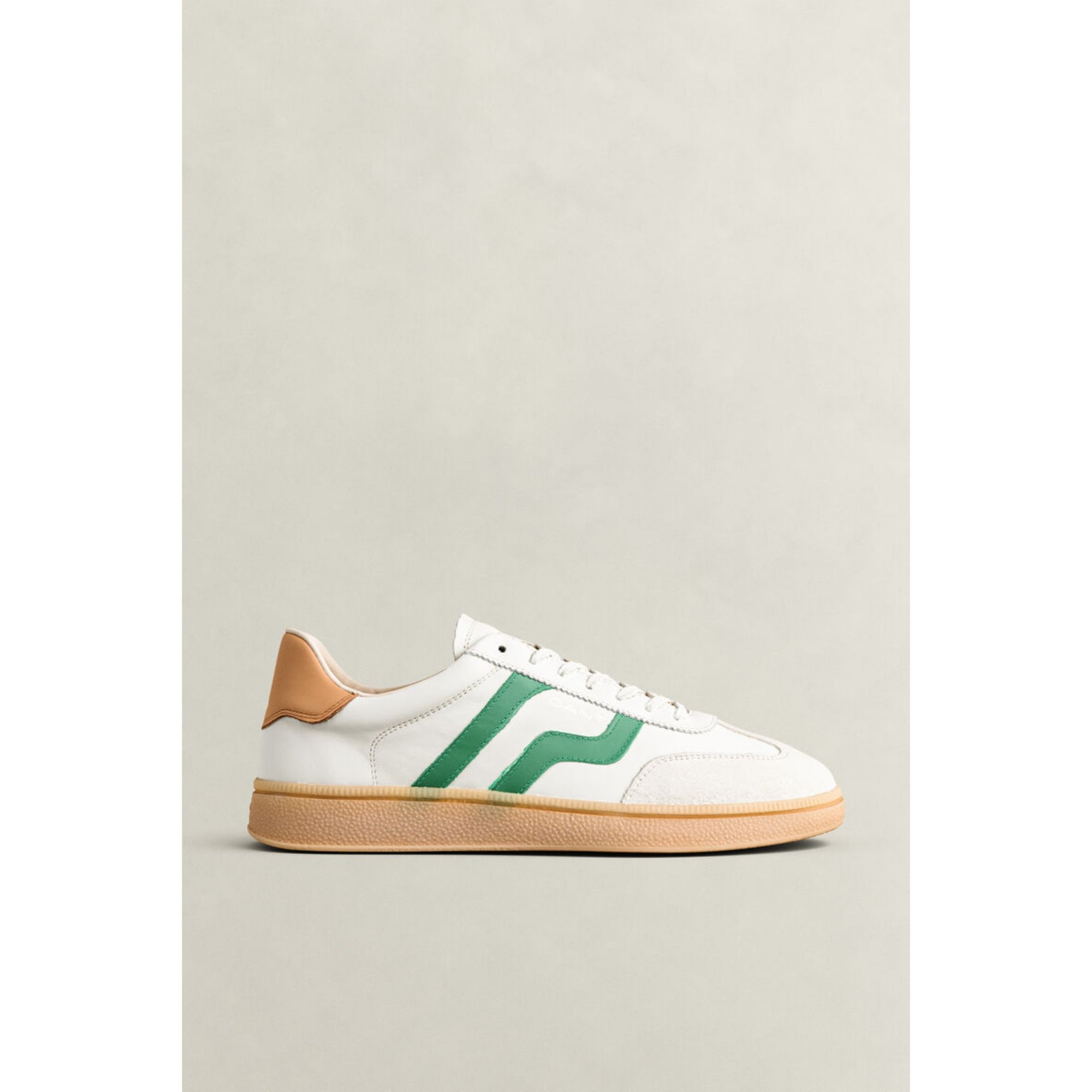 White sneaker with green logo and brown sole on a light gray background