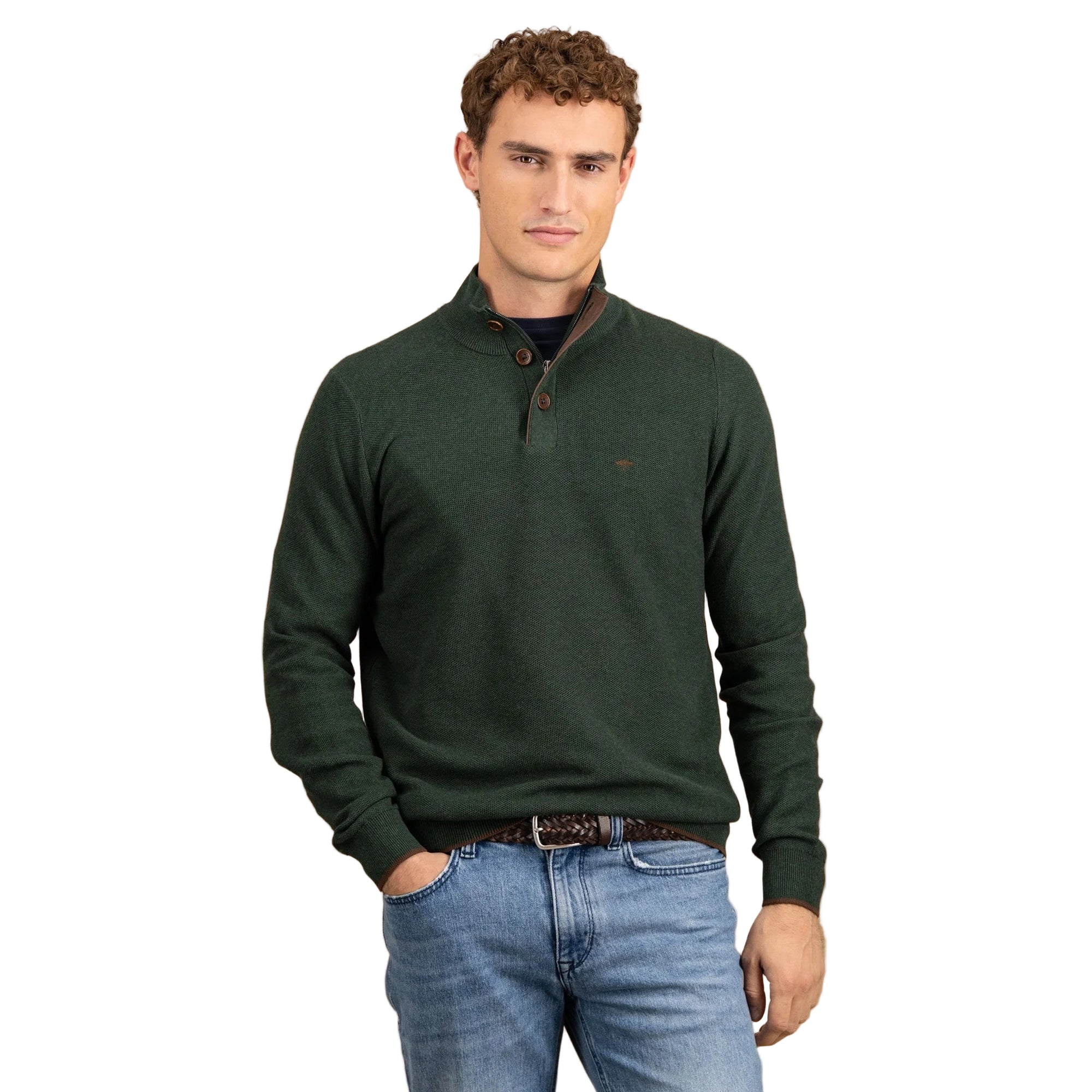 Man wearing a green sweater and blue jeans against a beige background