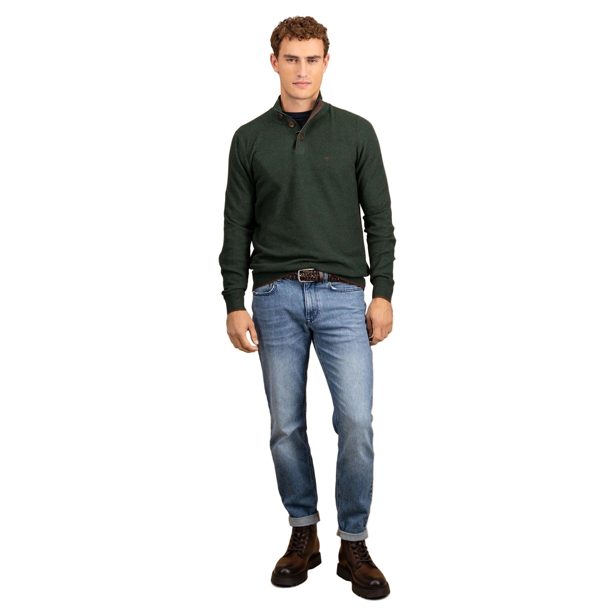 Man wearing a green sweater, blue jeans, and brown boots on a beige background