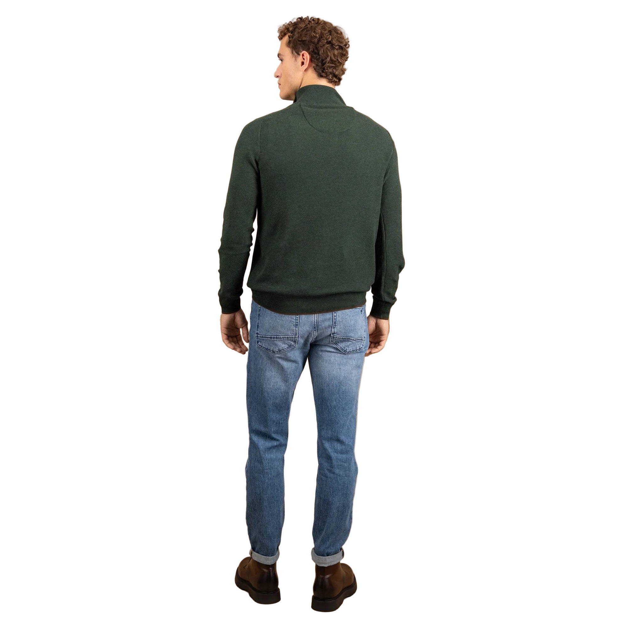 Man wearing a green sweater and blue jeans standing against a beige background