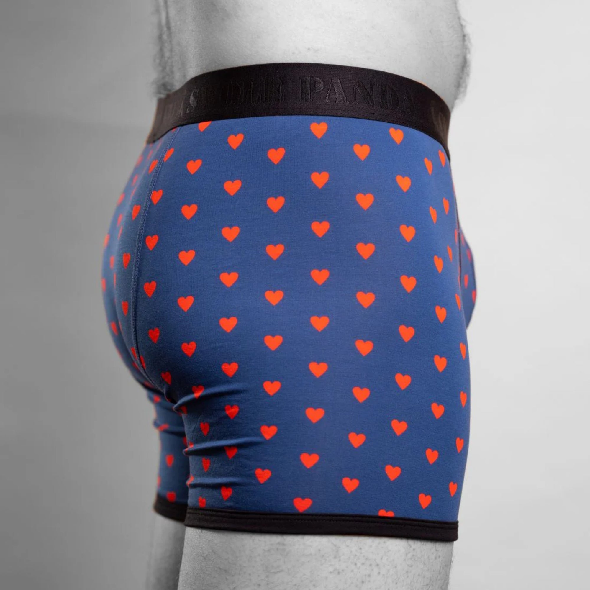 Blue boxer briefs with red heart pattern worn by a person on a gray background