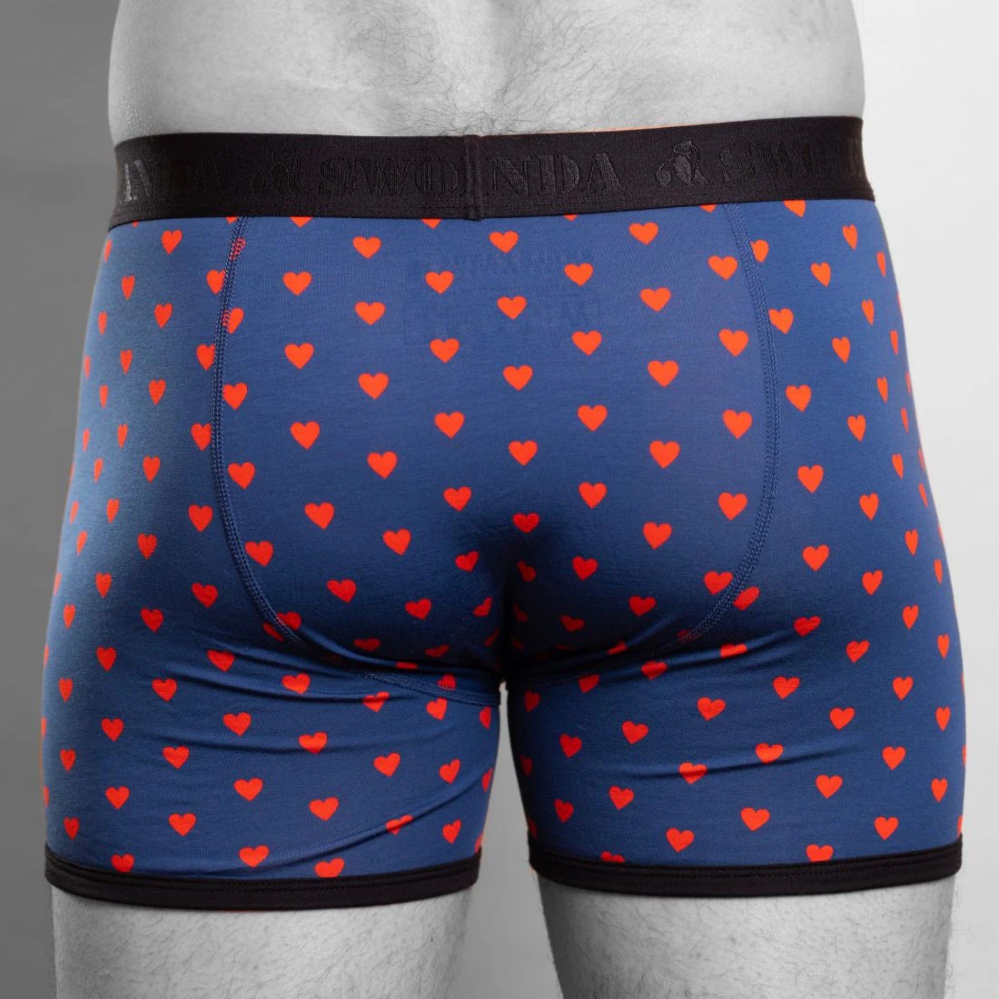 Blue boxer briefs with red heart pattern worn by a person on a gray background