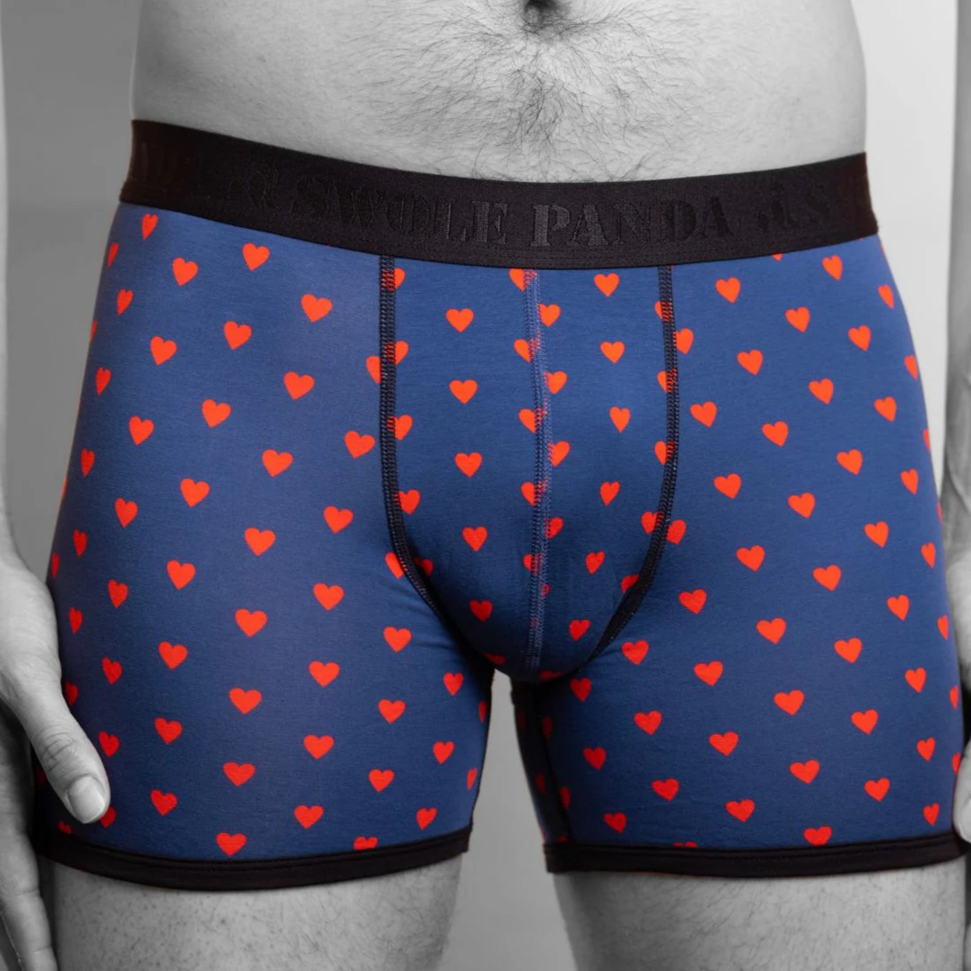 Blue boxer briefs with red heart pattern worn by a person on a gray background