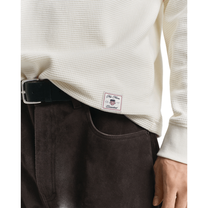 Close-up of a person wearing a white shirt and dark pants with a visible brand label.