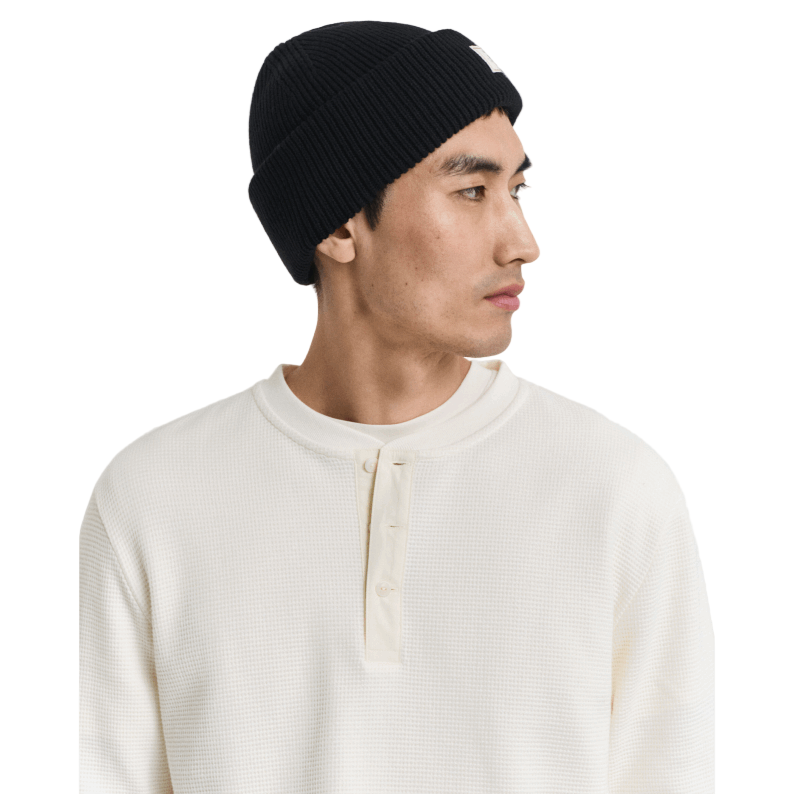 Man wearing a black knit beanie and white shirt against a plain background