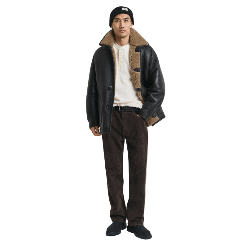 Man wearing a black leather jacket with shearling collar and brown pants on a white background