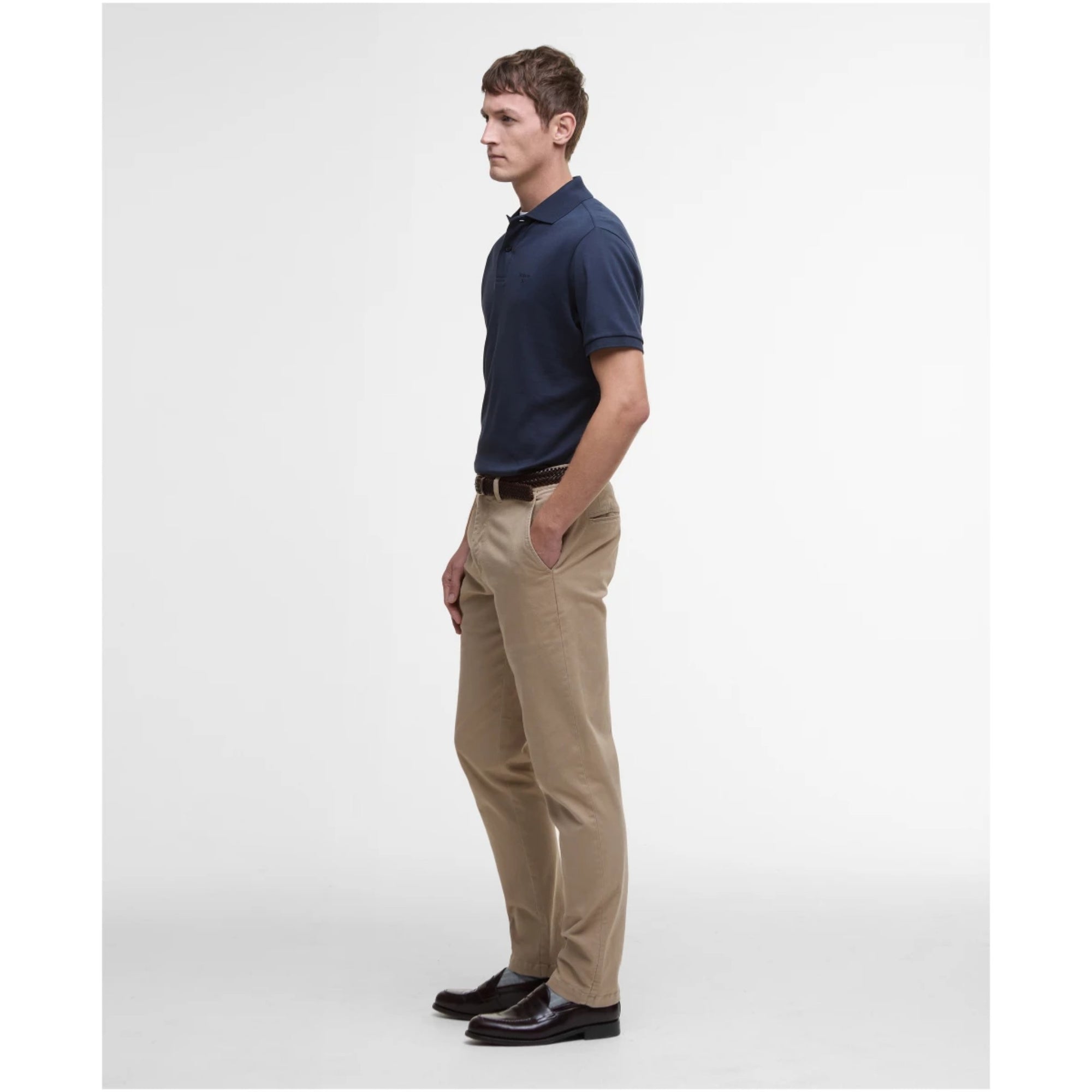 Man wearing a navy polo shirt, beige pants, and black shoes on a white background