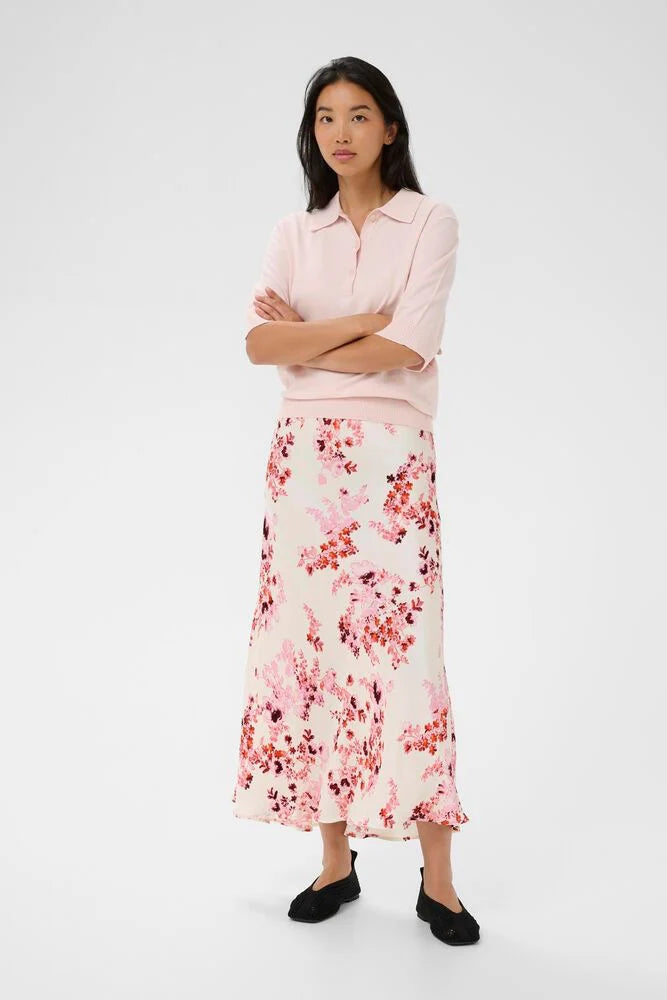 Woman wearing a light pink blouse and floral skirt on a white background