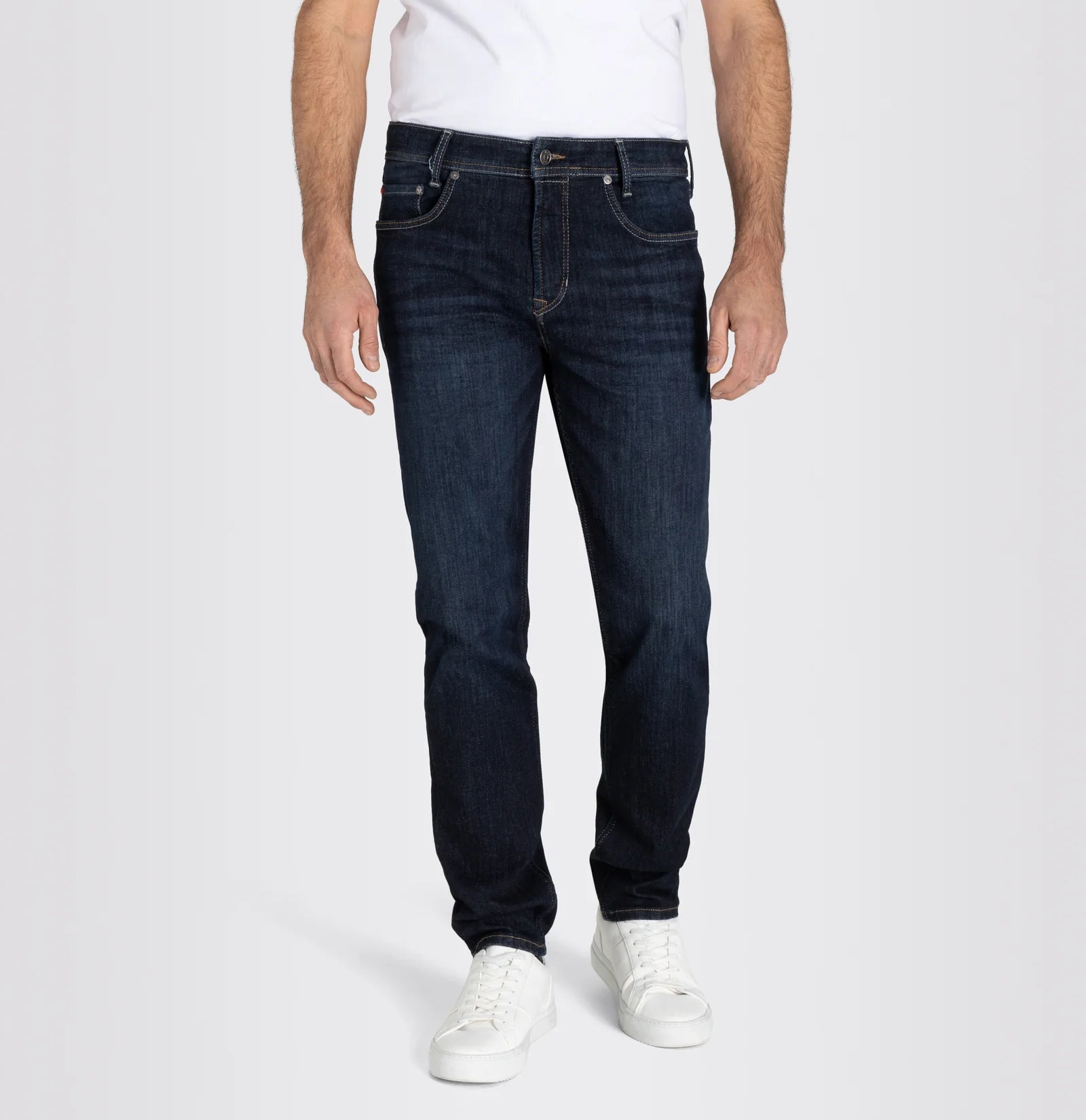 Person wearing dark blue jeans and white sneakers on a light gray background