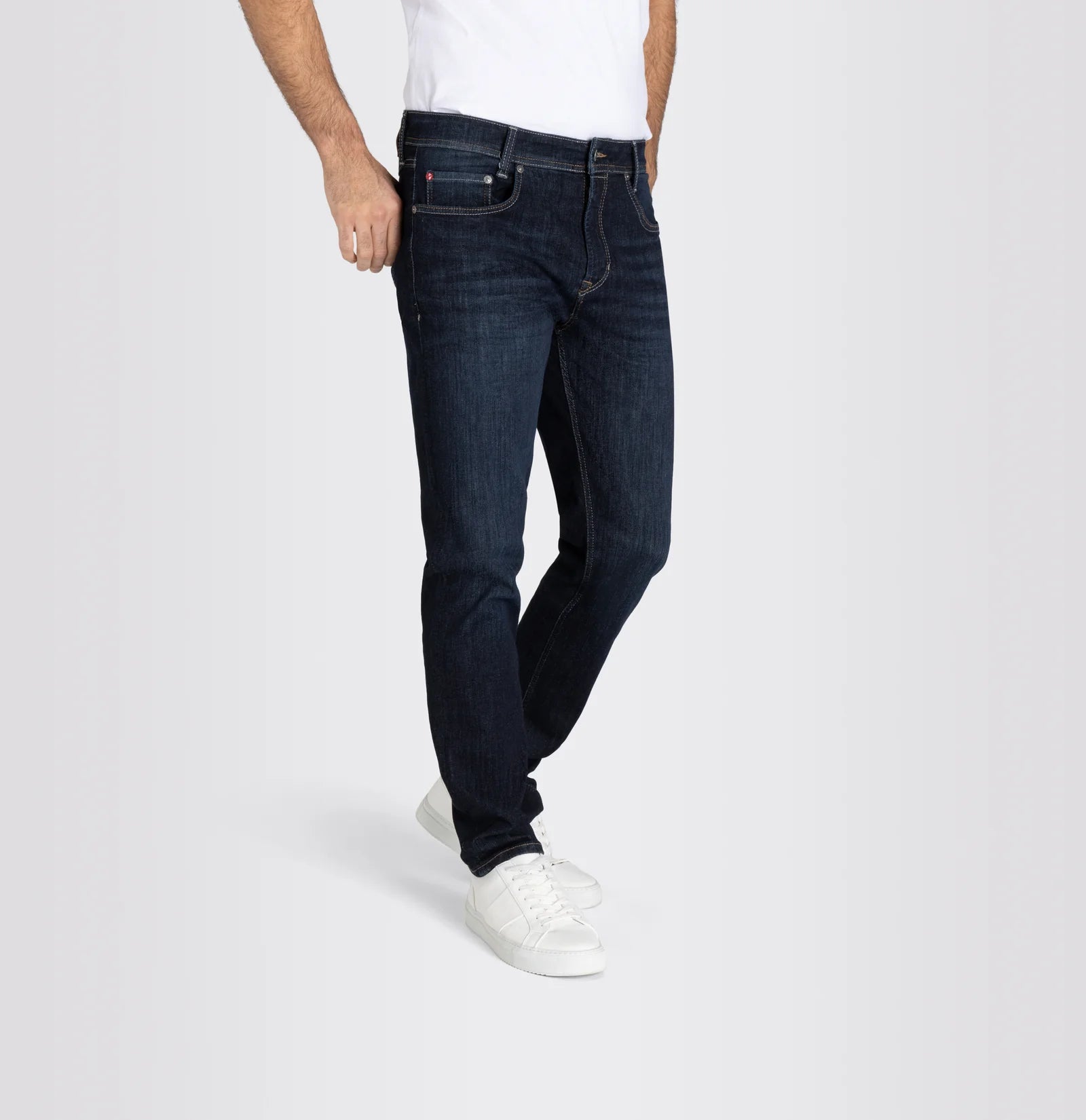 Person wearing dark blue jeans and white sneakers on a light gray background