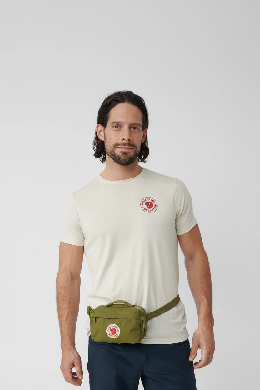 Man wearing a white t-shirt with a logo and a green bag on a light gray background