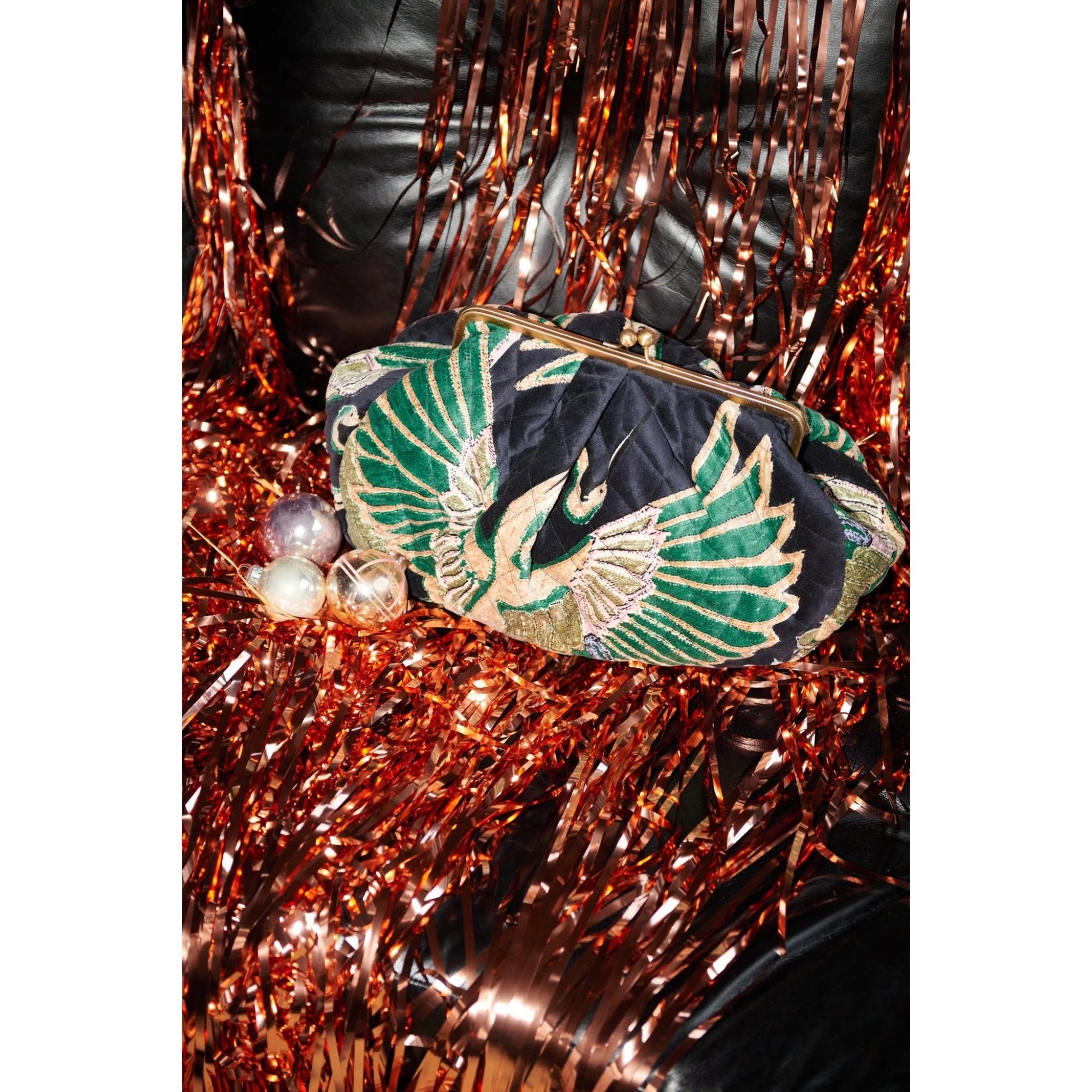 Embroidered clutch bag with green and gold design on a tinsel background