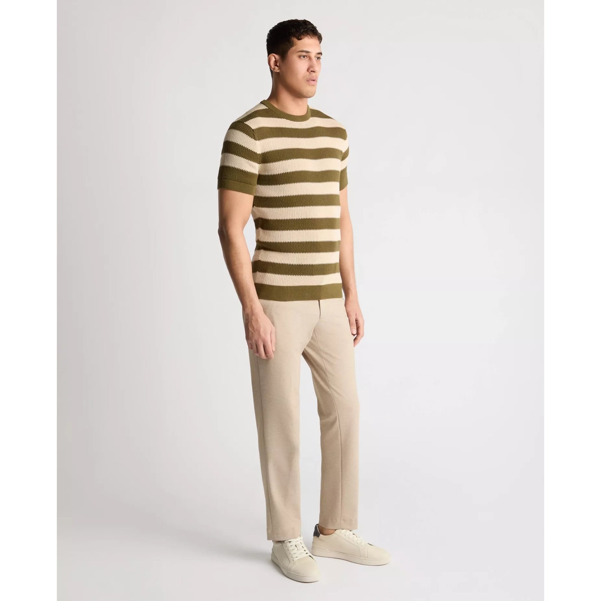Man wearing a striped sweater and beige pants on a light gray background