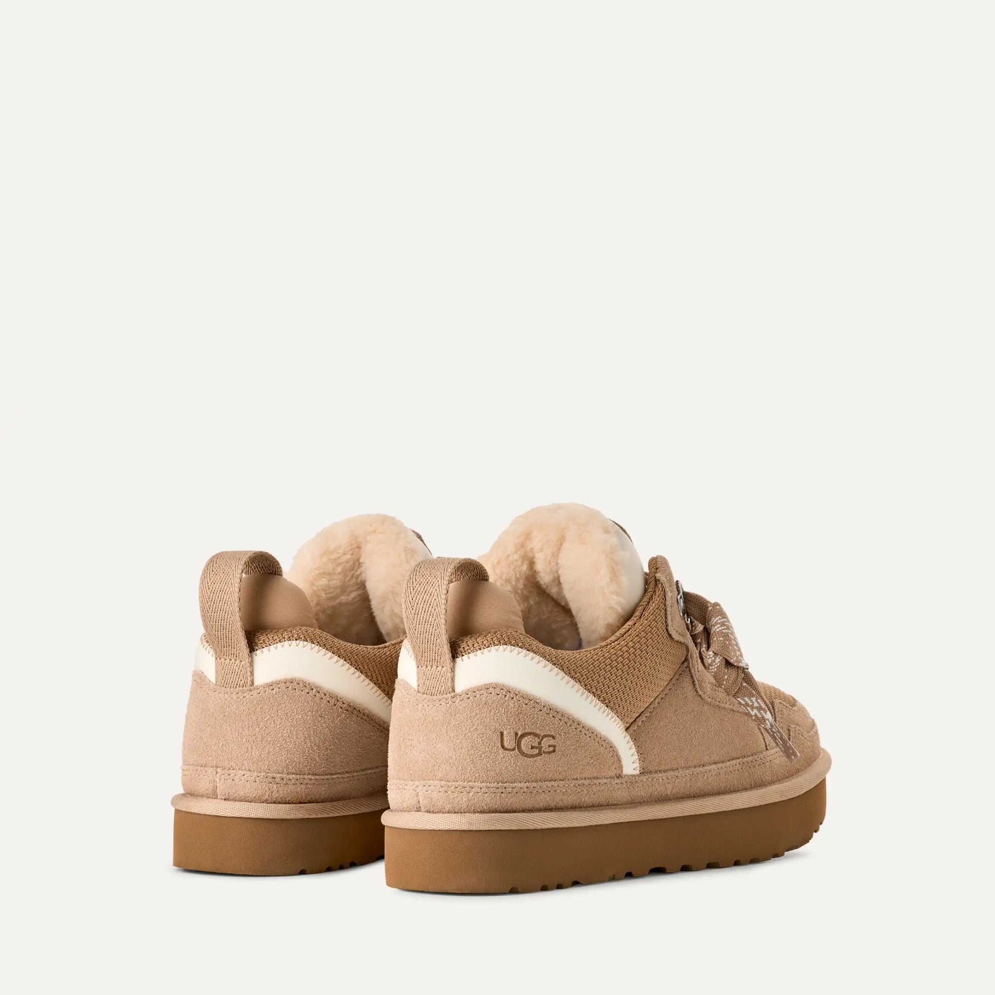 Pair of UGG Lowmel in Sand sneakers with fur accents on a light beige background