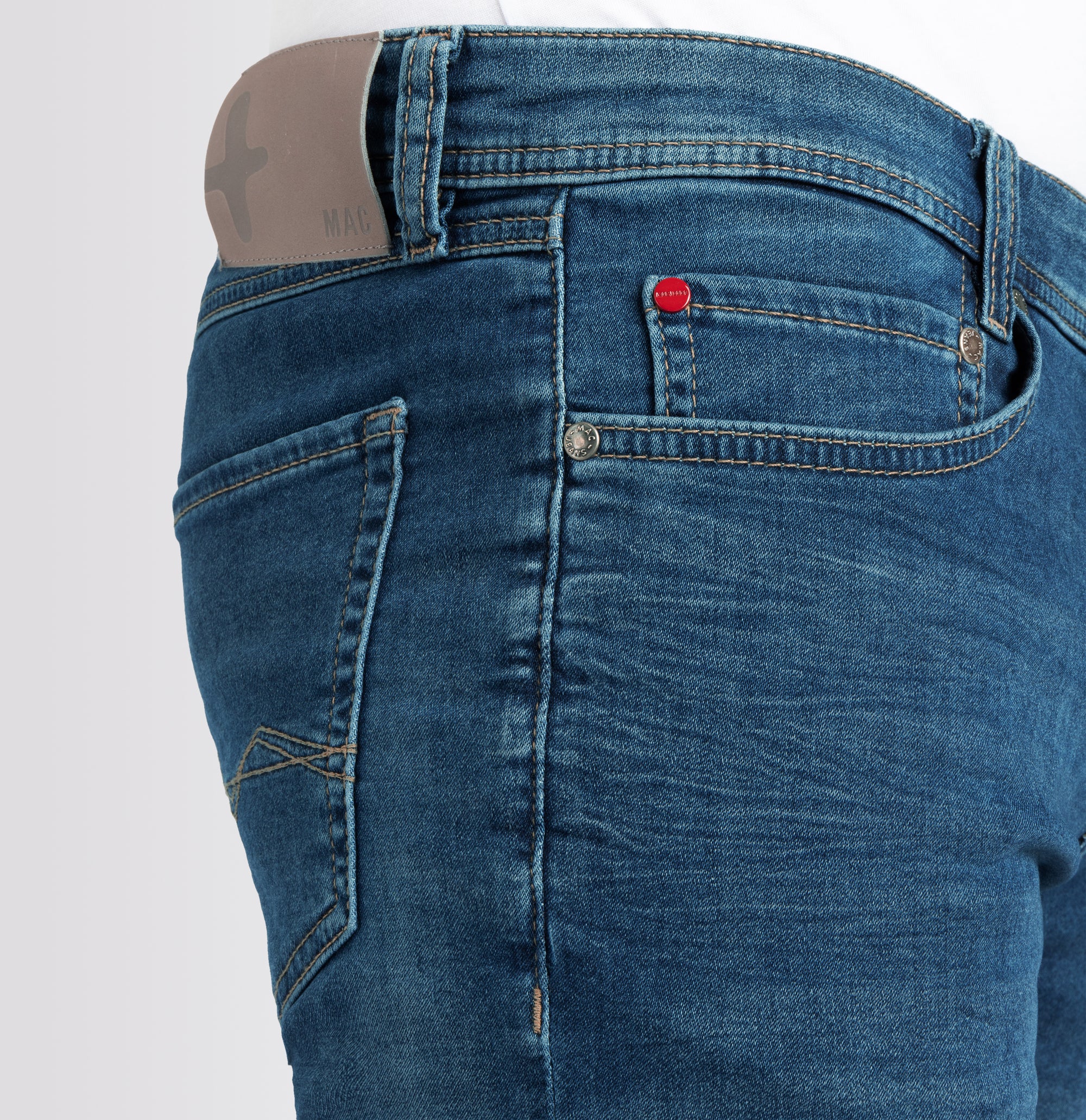 Close-up of blue jeans with a red button on a light gray background
