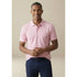 Man wearing a pink polo shirt and navy pants against a beige background