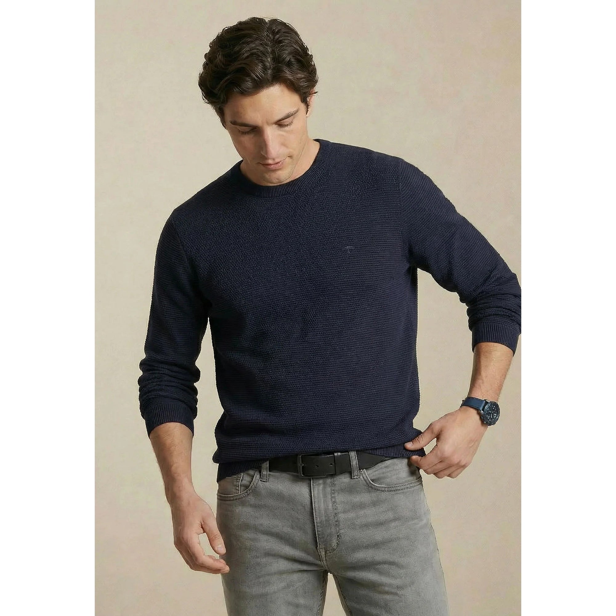 Man wearing a navy sweater and gray jeans against a beige background