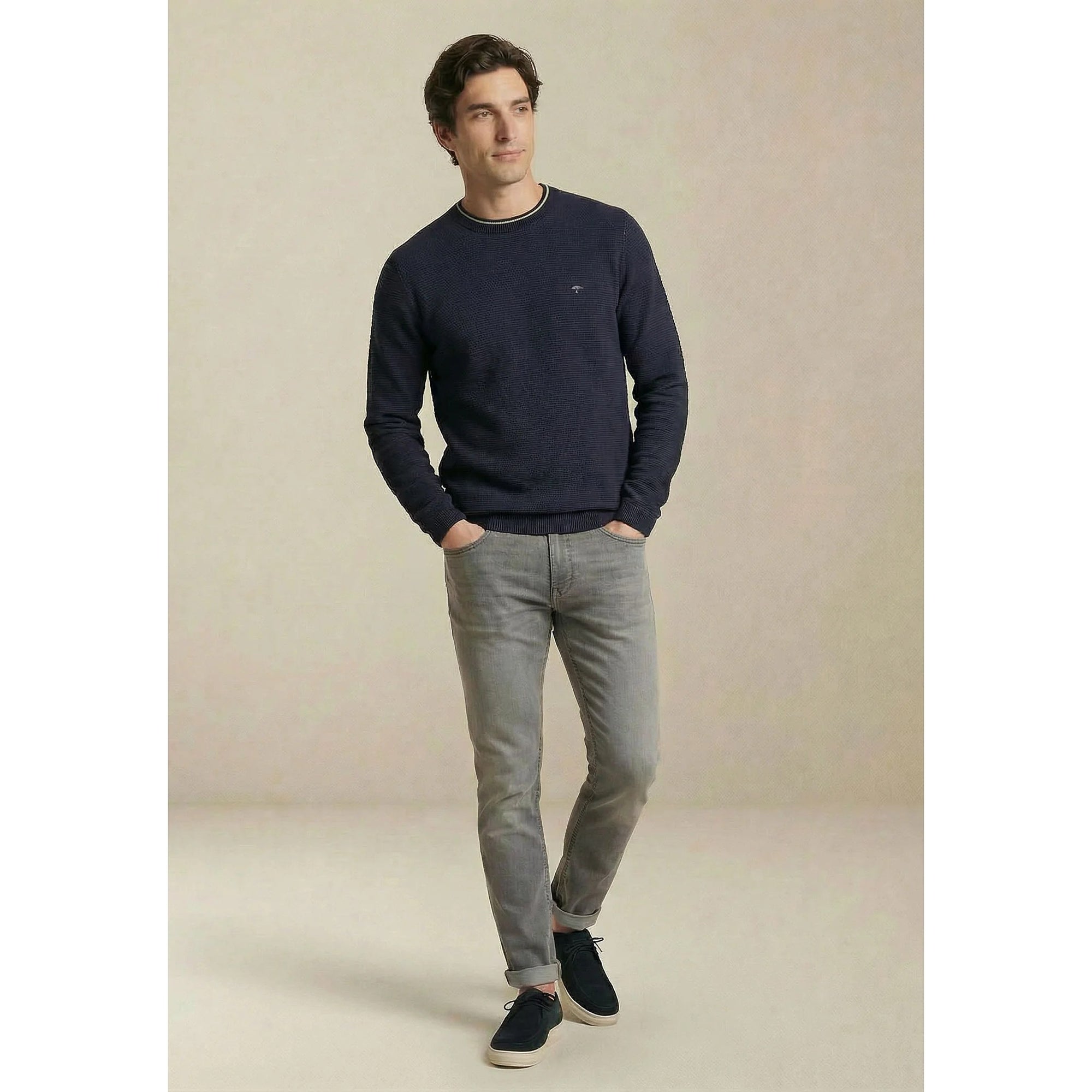 Man wearing a navy sweater and light gray jeans against a neutral background