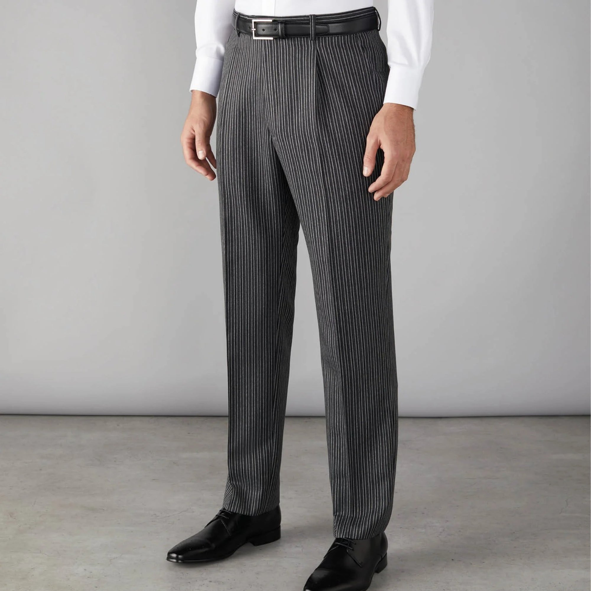Person wearing gray pinstripe dress pants with a white shirt and black shoes on a plain background