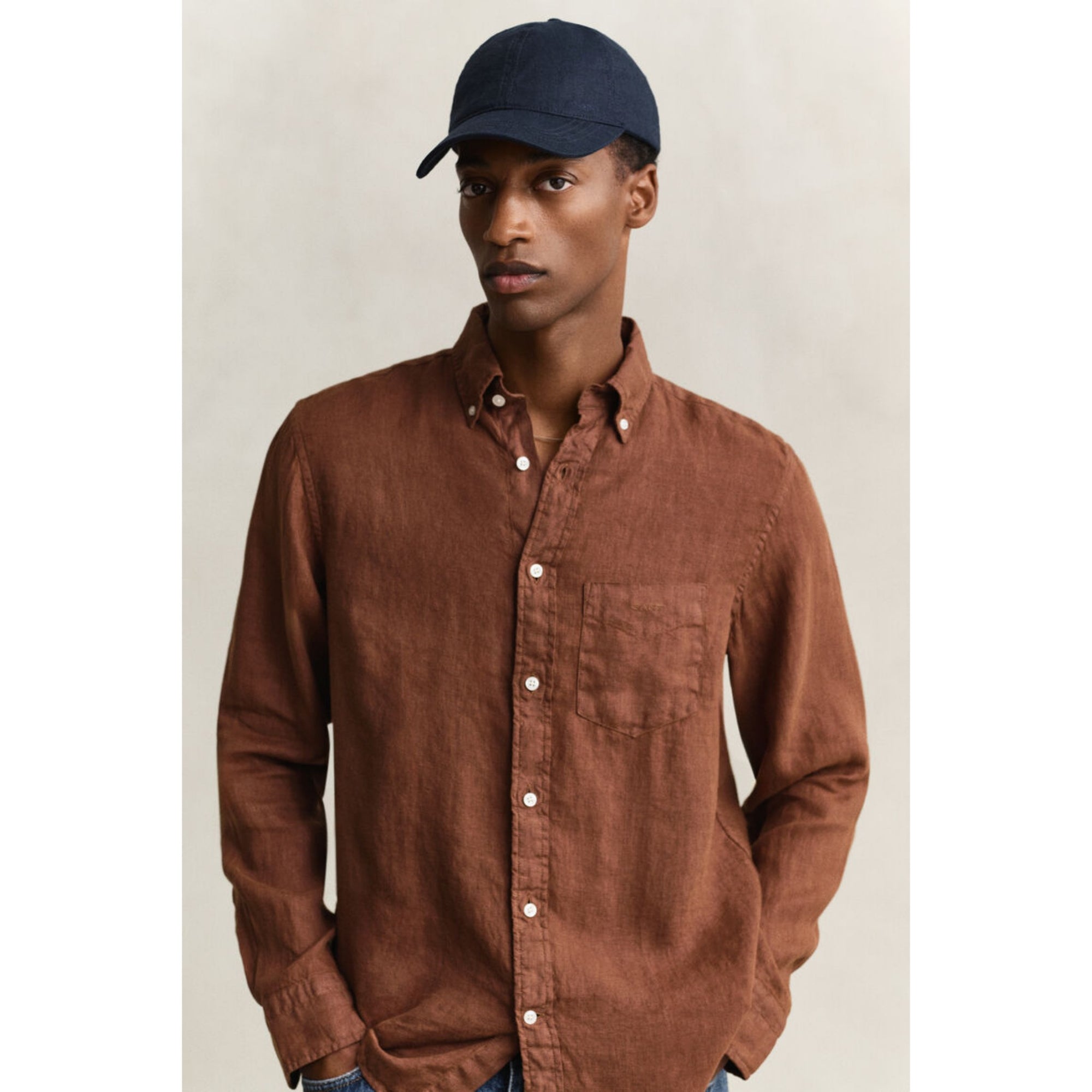 Man wearing a brown shirt and navy cap against a neutral background