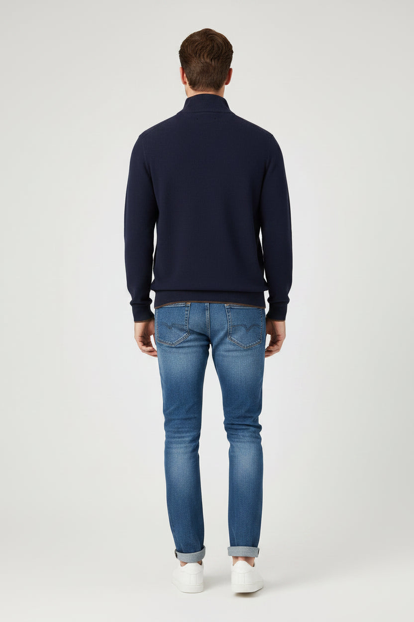A man modeling a navy blue quarter-zip pullover sweater with blue jeans and white sneakers, standing against a light gray studio background.