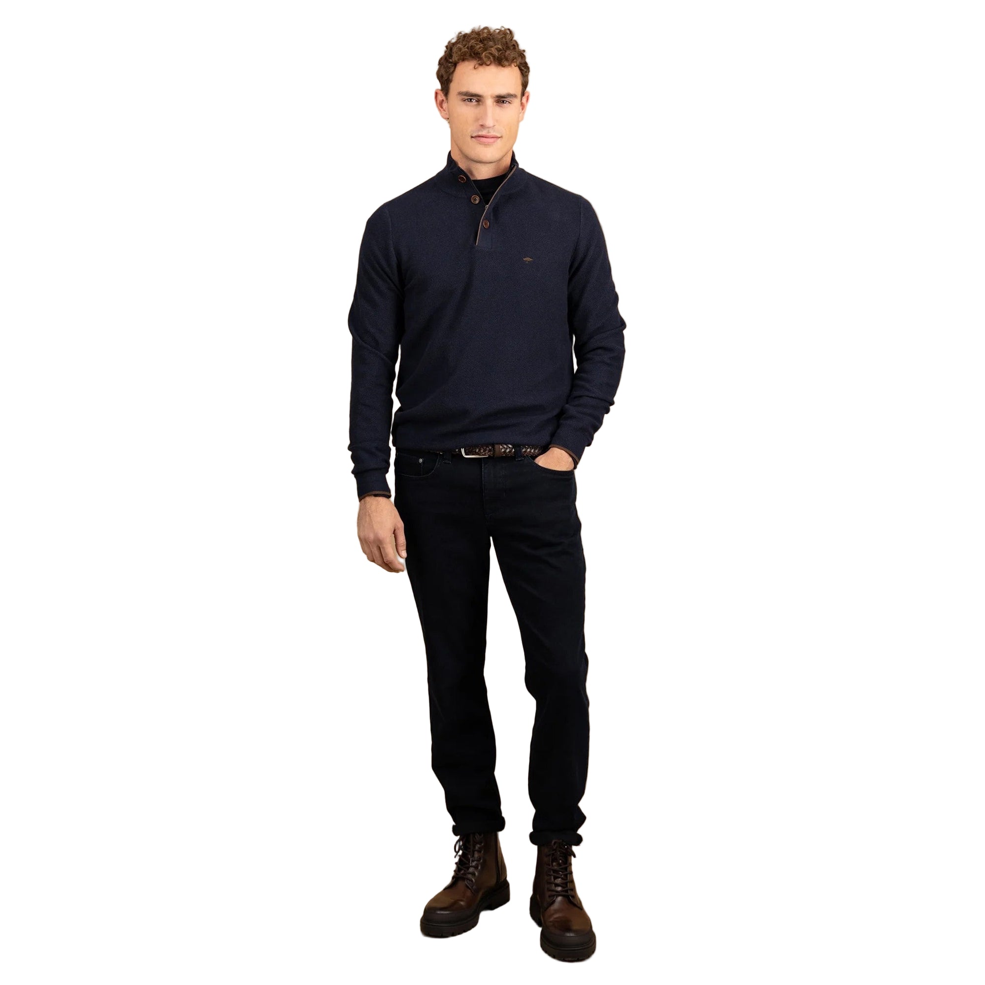 Man wearing a navy sweater, black jeans, and brown boots on a beige background