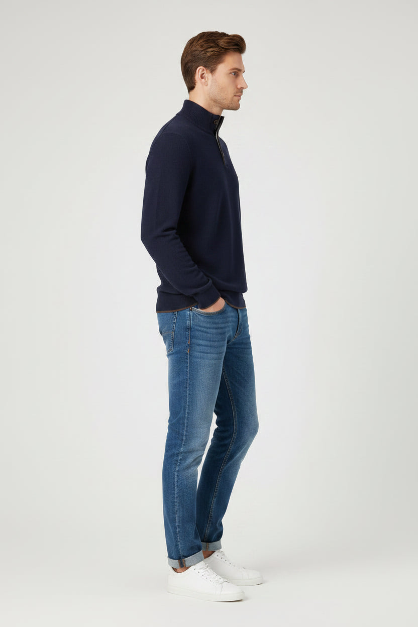 A man modeling a navy blue quarter-zip pullover sweater with blue jeans and white sneakers, standing against a light gray studio background.