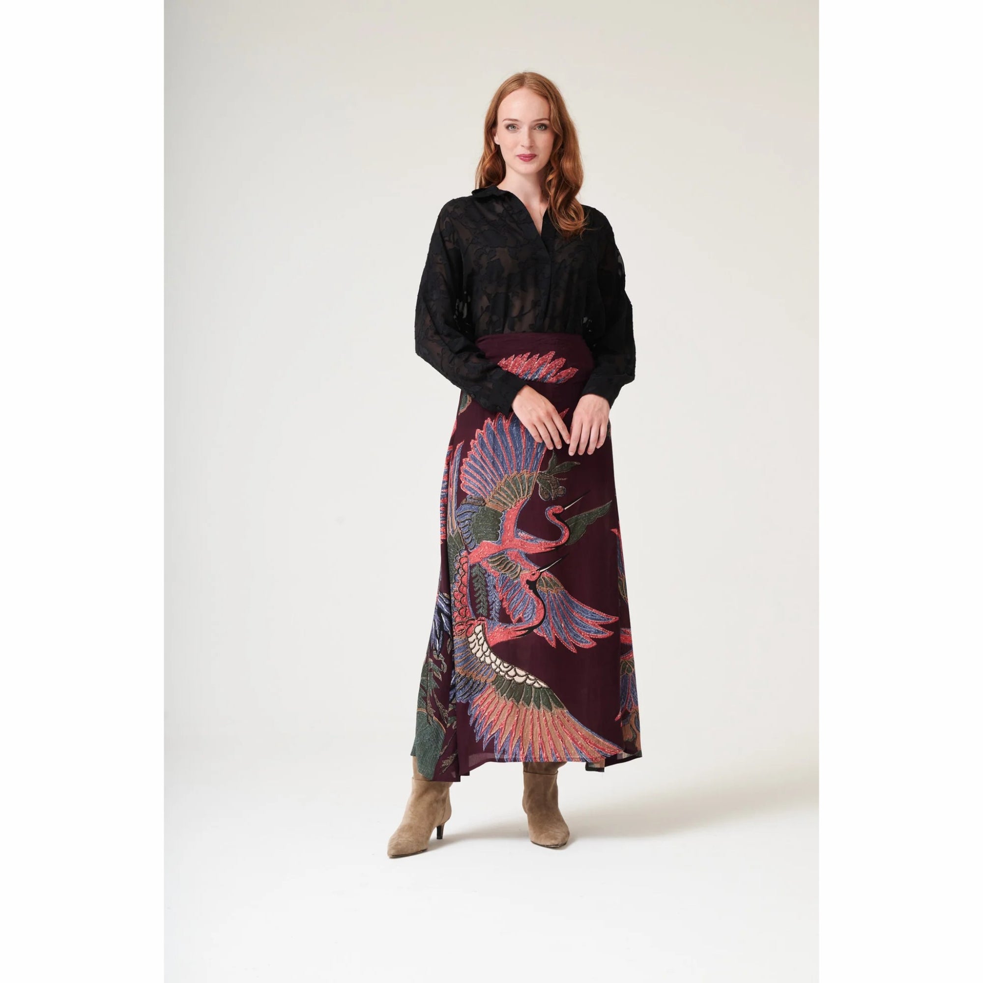 Woman wearing a black blouse and a long, patterned skirt with a peacock design on a white background