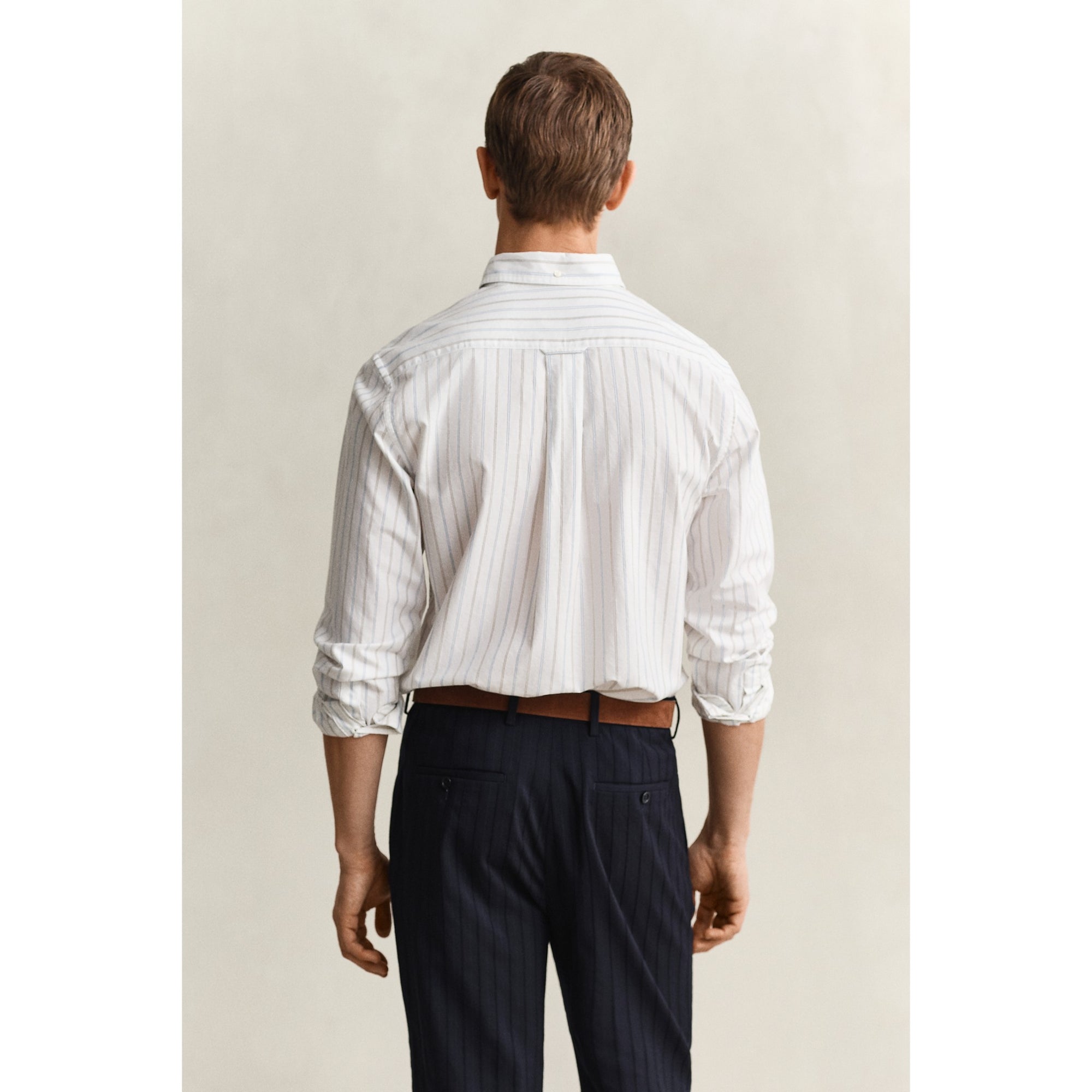 Man wearing a white striped shirt and dark pants against a plain background