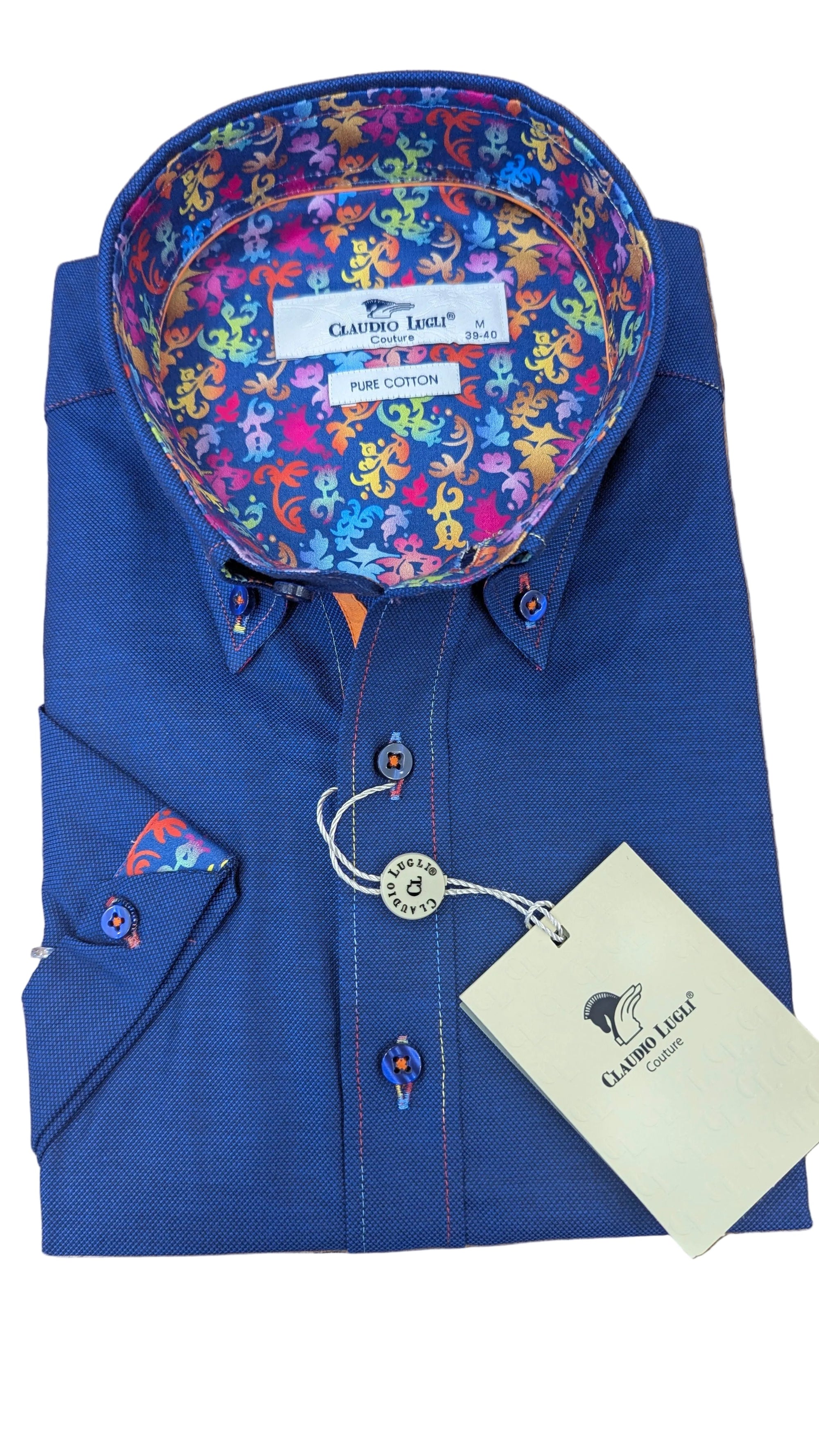 Folded blue shirt with colorful patterned collar on a wooden surface, featuring a brand tag.