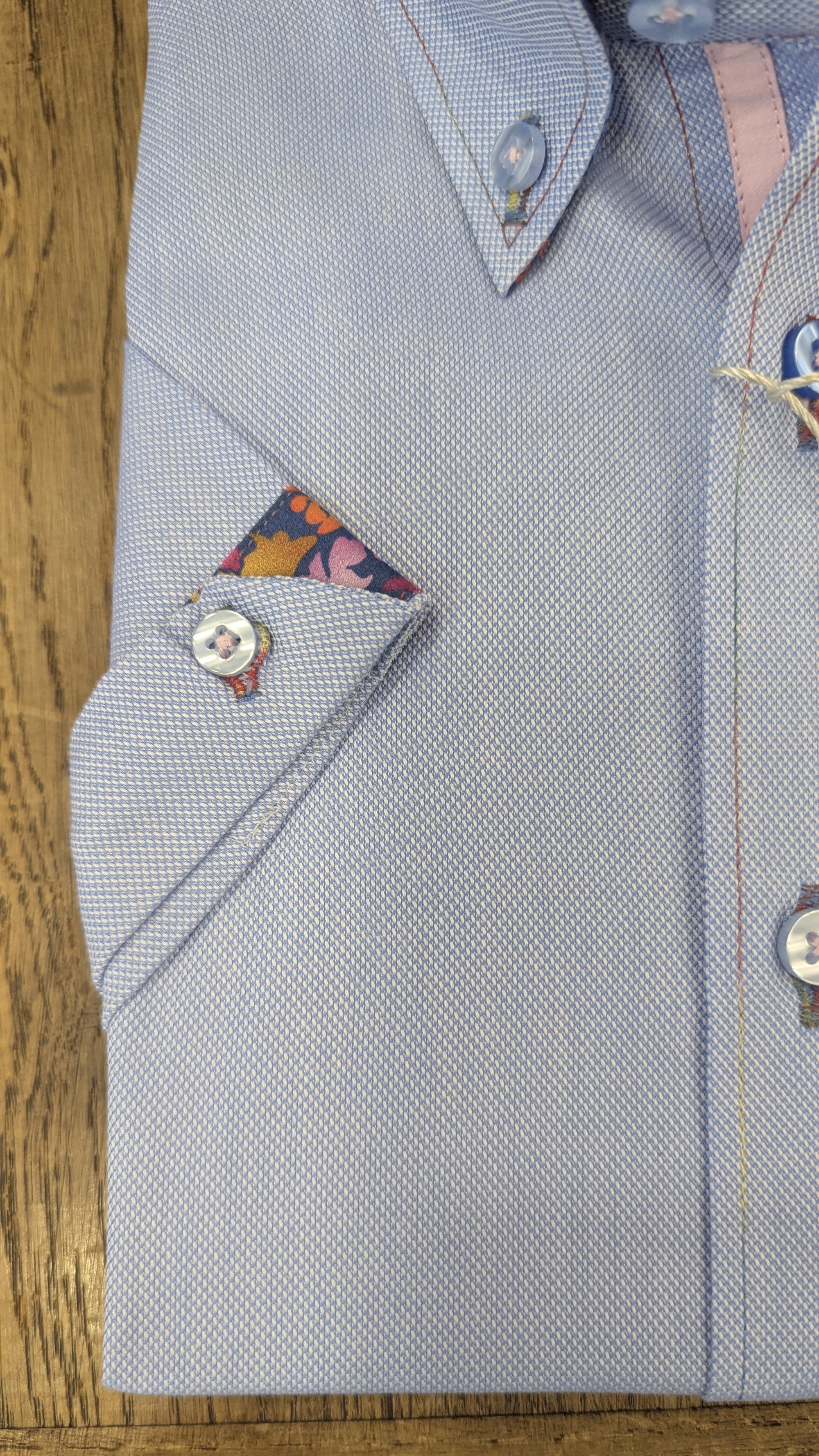 Folded light blue dress shirt with a colorful pocket square on a wooden surface